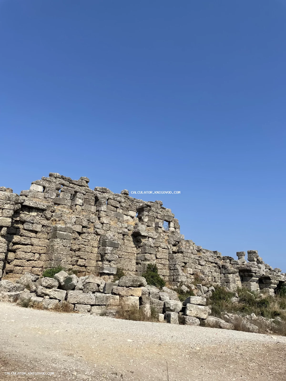 Остатки массивной стены из крупных каменных блоков на фоне ясного голубого неба