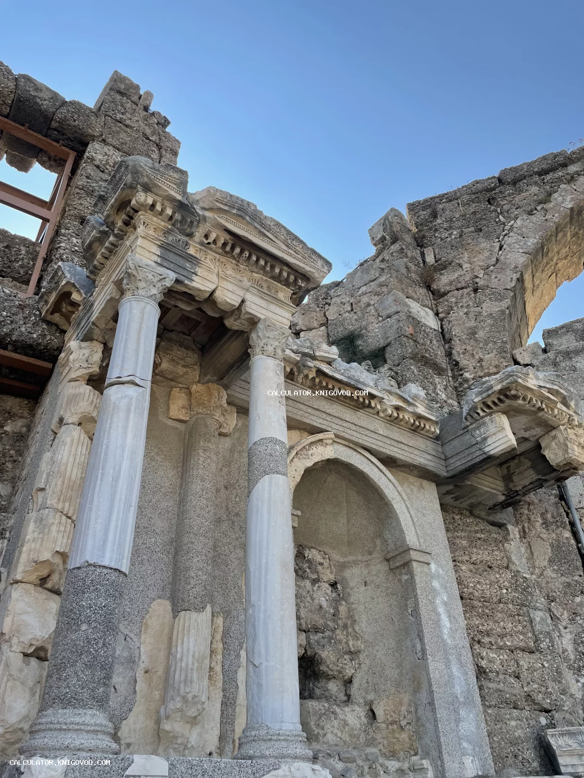 Руины античного здания с сохранившимися мраморными колоннами, коринфскими капителями и каменными сводами под ясным небом.