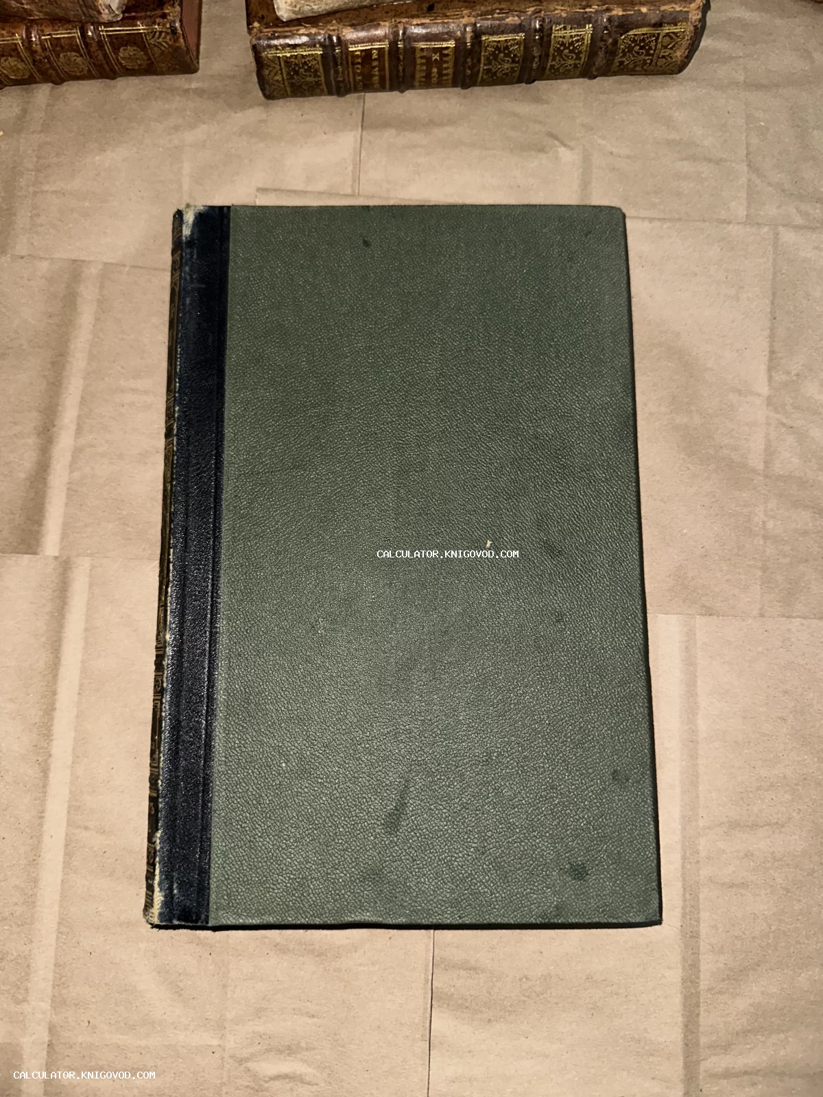 Антикварная книга с темно-зеленой фактурной обложкой и темным корешком на фоне других старых томов.