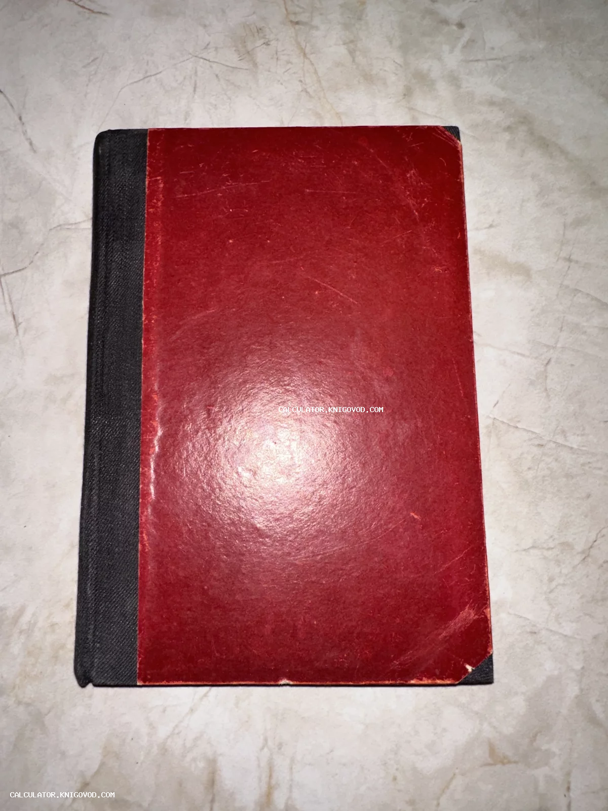 Антикварная книга с темно-красной обложкой и черным тканевым корешком на мраморной поверхности