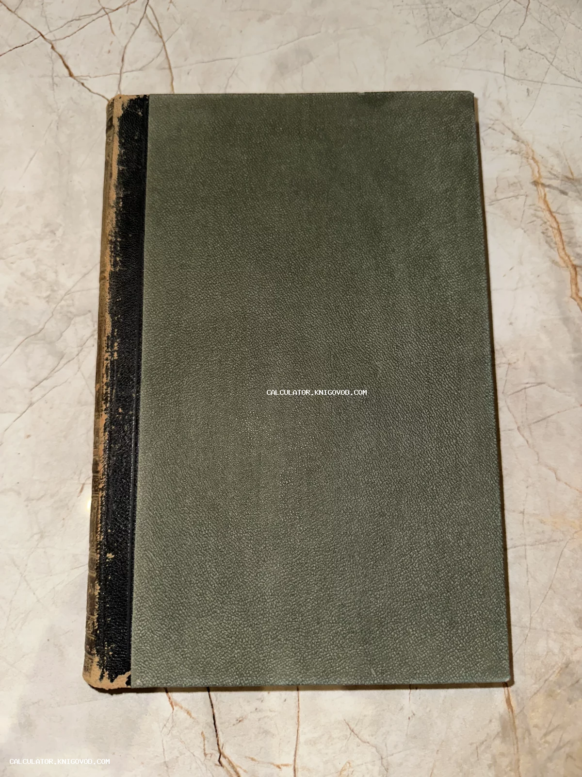 Старинная книга с серо-зеленой фактурной обложкой и потертым черным корешком на светлом фоне.