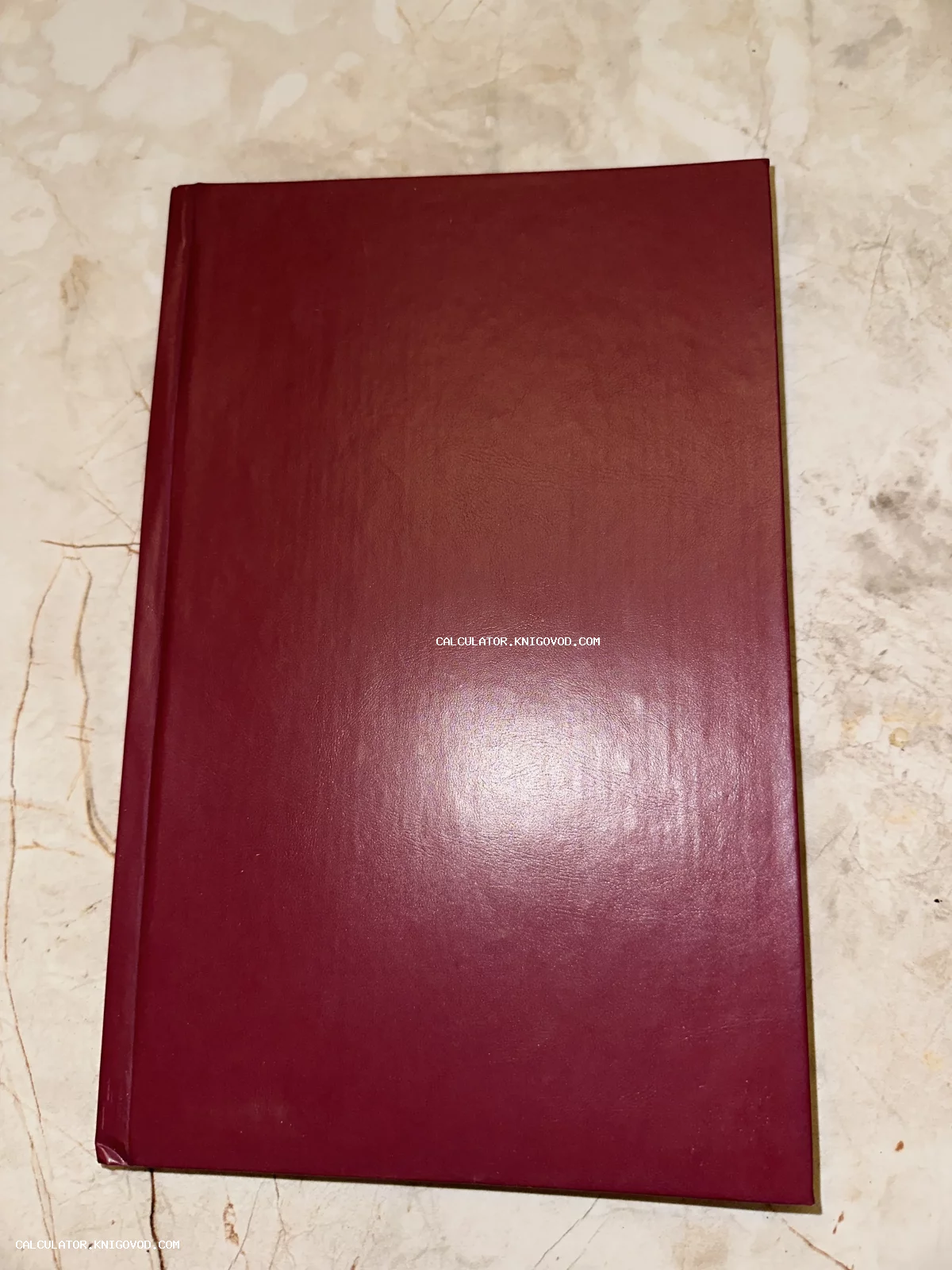 Старинная книга в твердом бордовом переплете на мраморной поверхности.