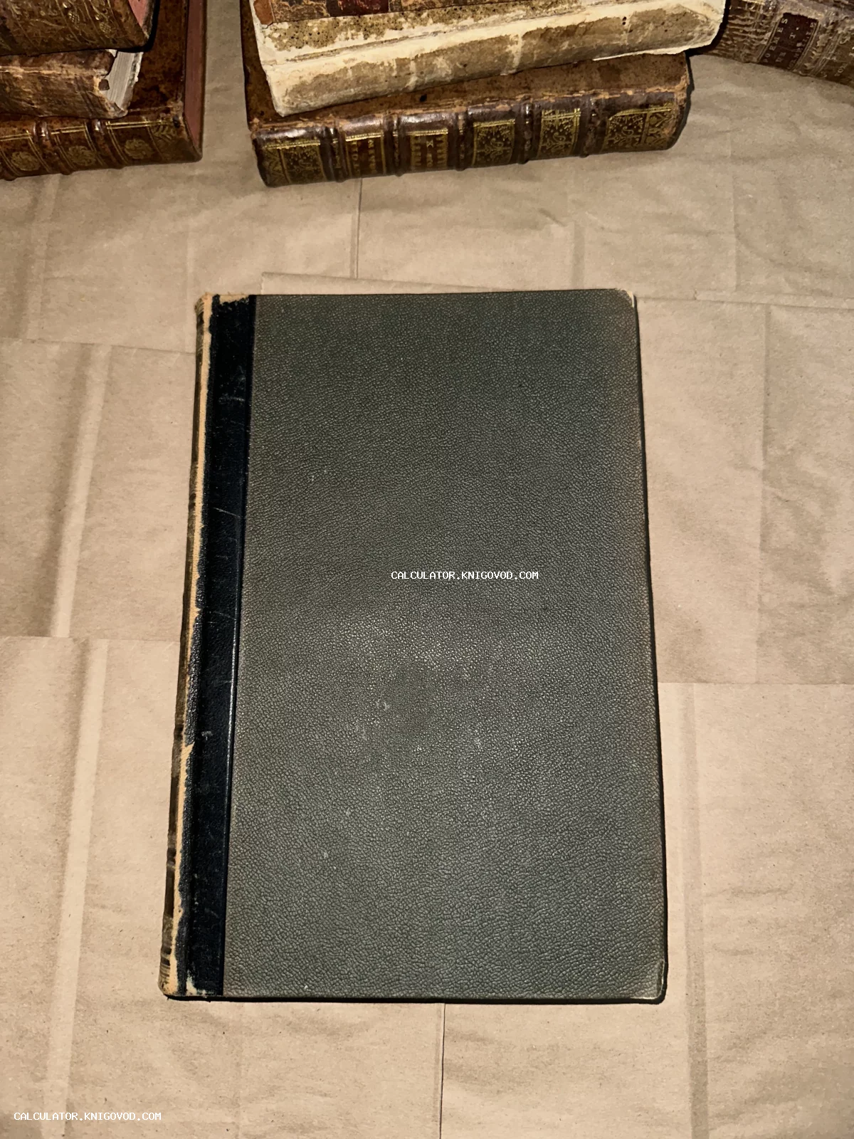 Антикварная книга с темно-зеленой фактурной обложкой и черным корешком на фоне других старых томов.