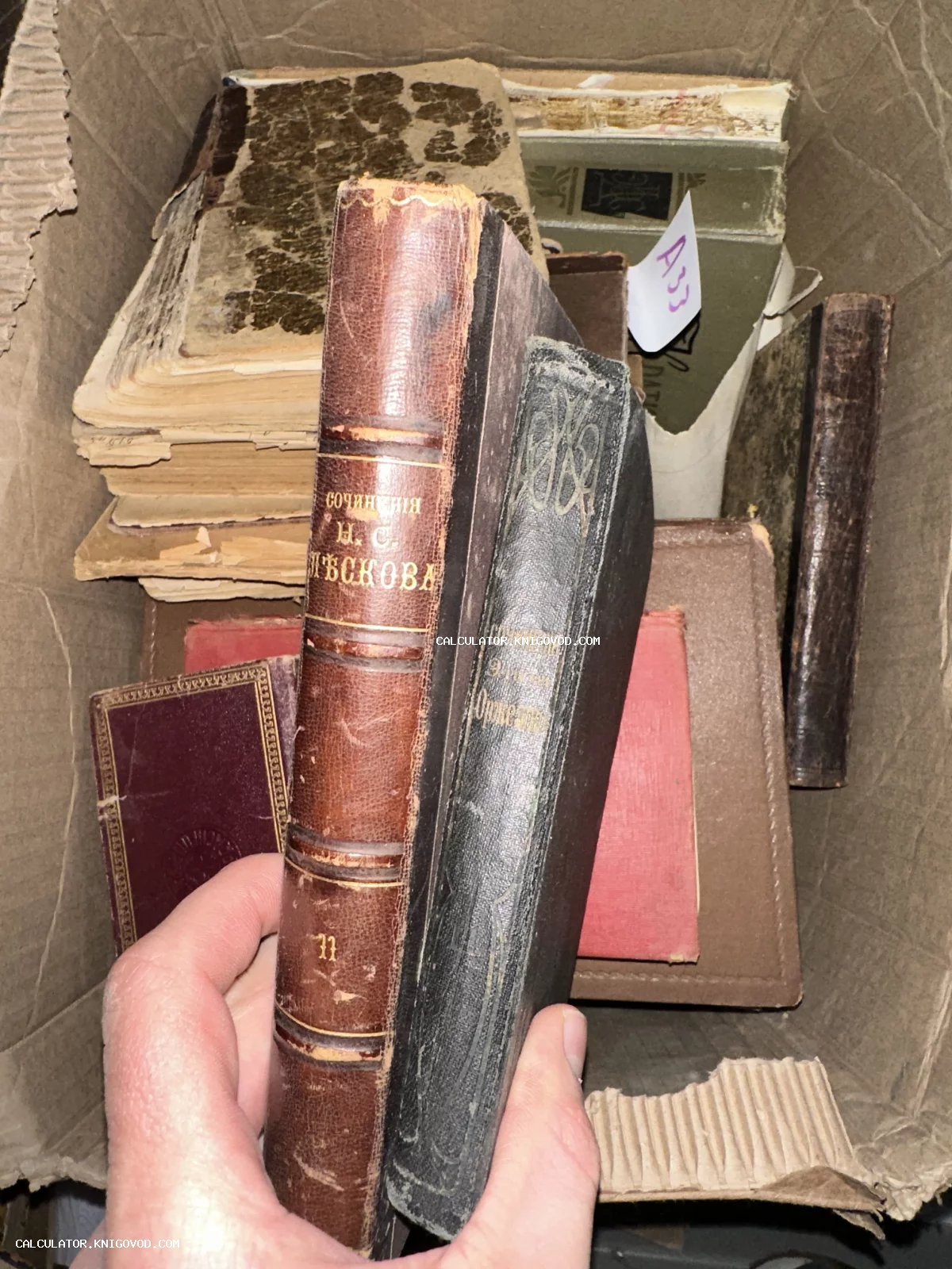 Старинные книги в картонной коробке, рука держит 11 том сочинений Лескова в кожаном переплете с золотым тиснением.