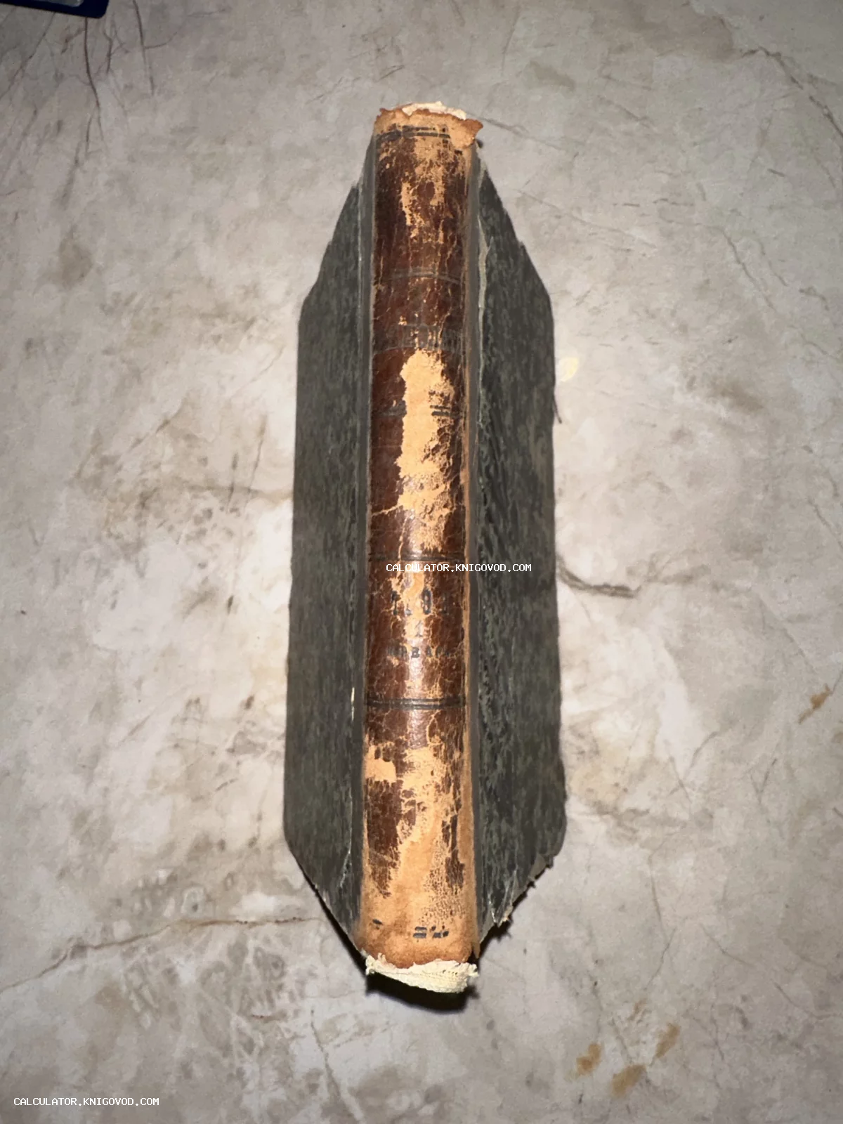 Корешок старинной книги в потертом кожаном переплете на фоне мраморной поверхности.