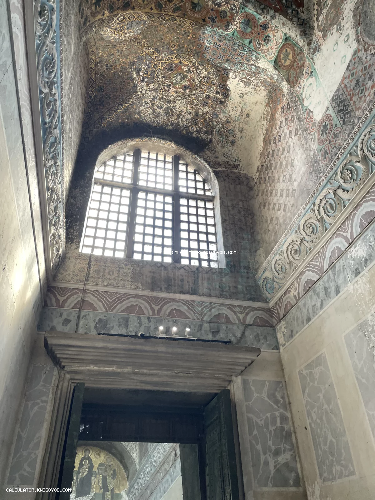 Интерьер старинного храма с высокими сводчатыми потолками, украшенными сложным геометрическим орнаментом, и массивным арочным окном.