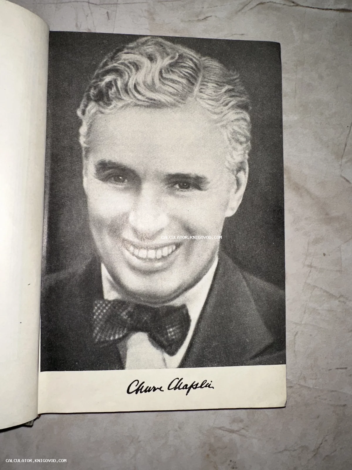 Черно-белая фотография Чарли Чаплина на странице старой книги с факсимиле его подписи внизу.