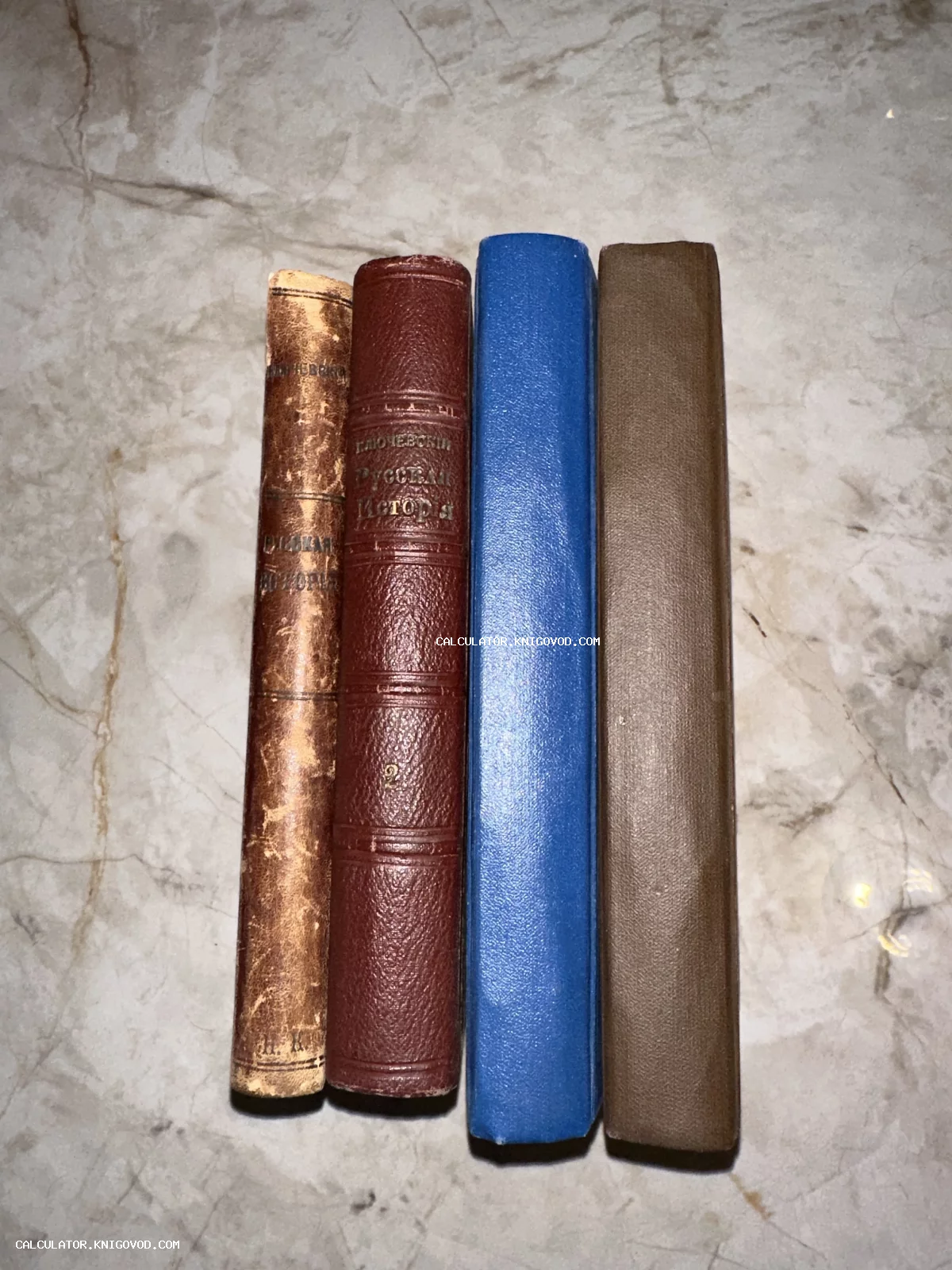 Корешки четырех старинных книг в кожаных и тканевых переплетах, включая издания Ключевского, на мраморной поверхности.