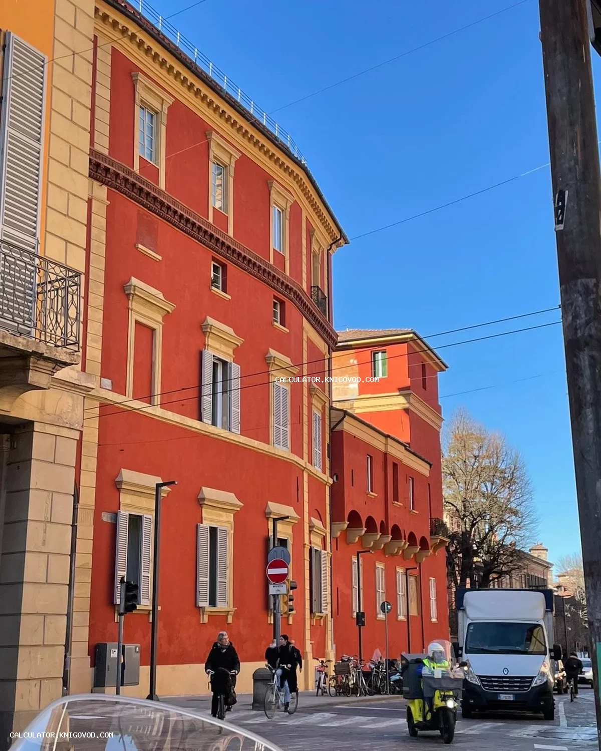 Фасад исторического красного здания с желтой отделкой и белыми ставнями на фоне ярко-синего неба.