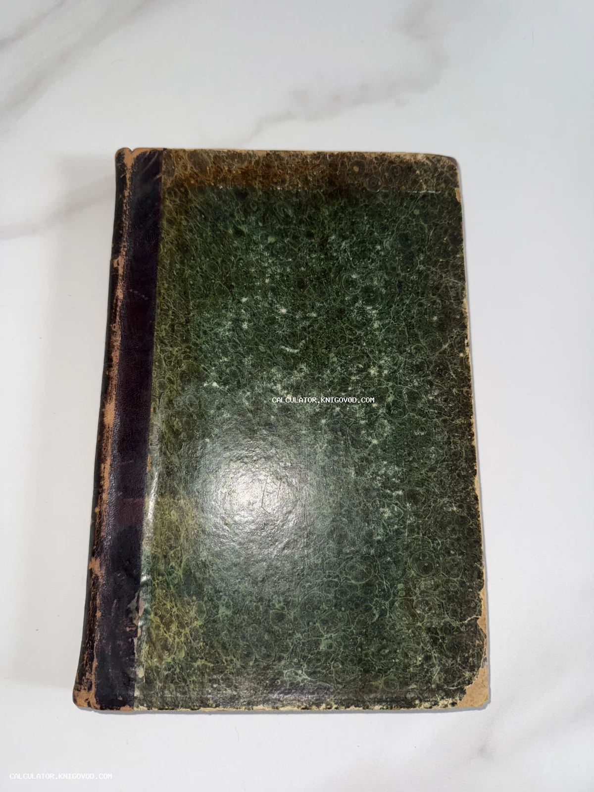 Старинная книга с обложкой из зеленой мраморной бумаги и темным кожаным корешком на светлом фоне.