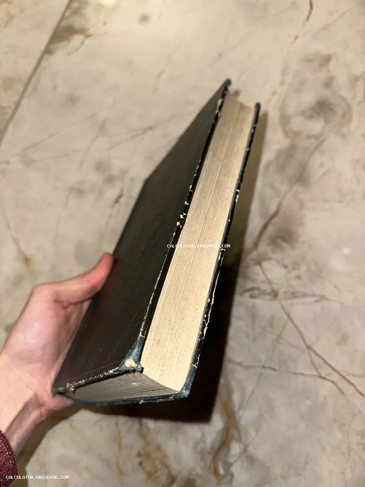 Старинная книга с темной обложкой и пожелтевшими страницами в руке на фоне мраморного пола