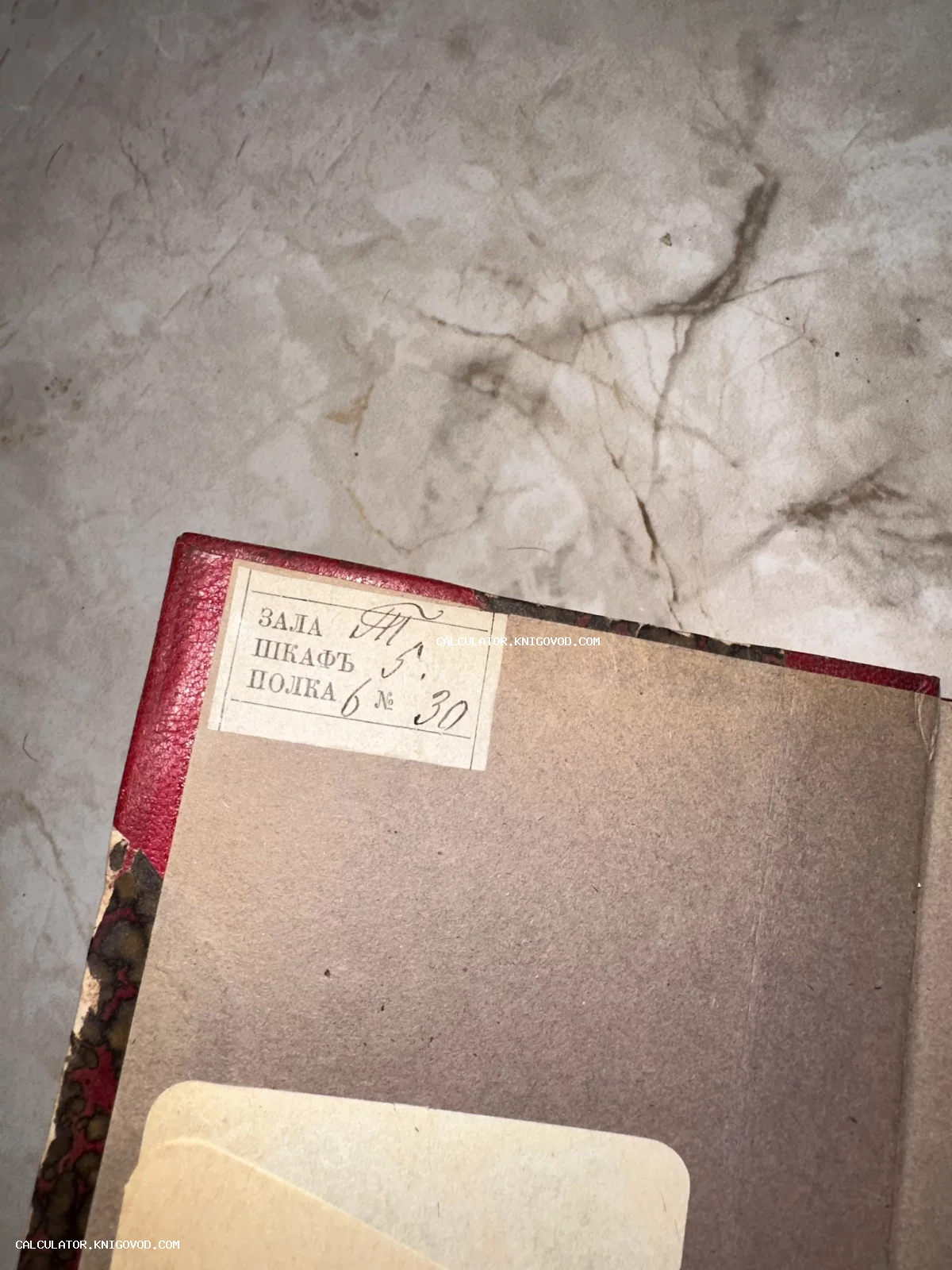 Крупный план старинного бумажного ярлыка в углу книги с рукописными пометками о расположении в библиотеке: зала, шкаф и полка.
