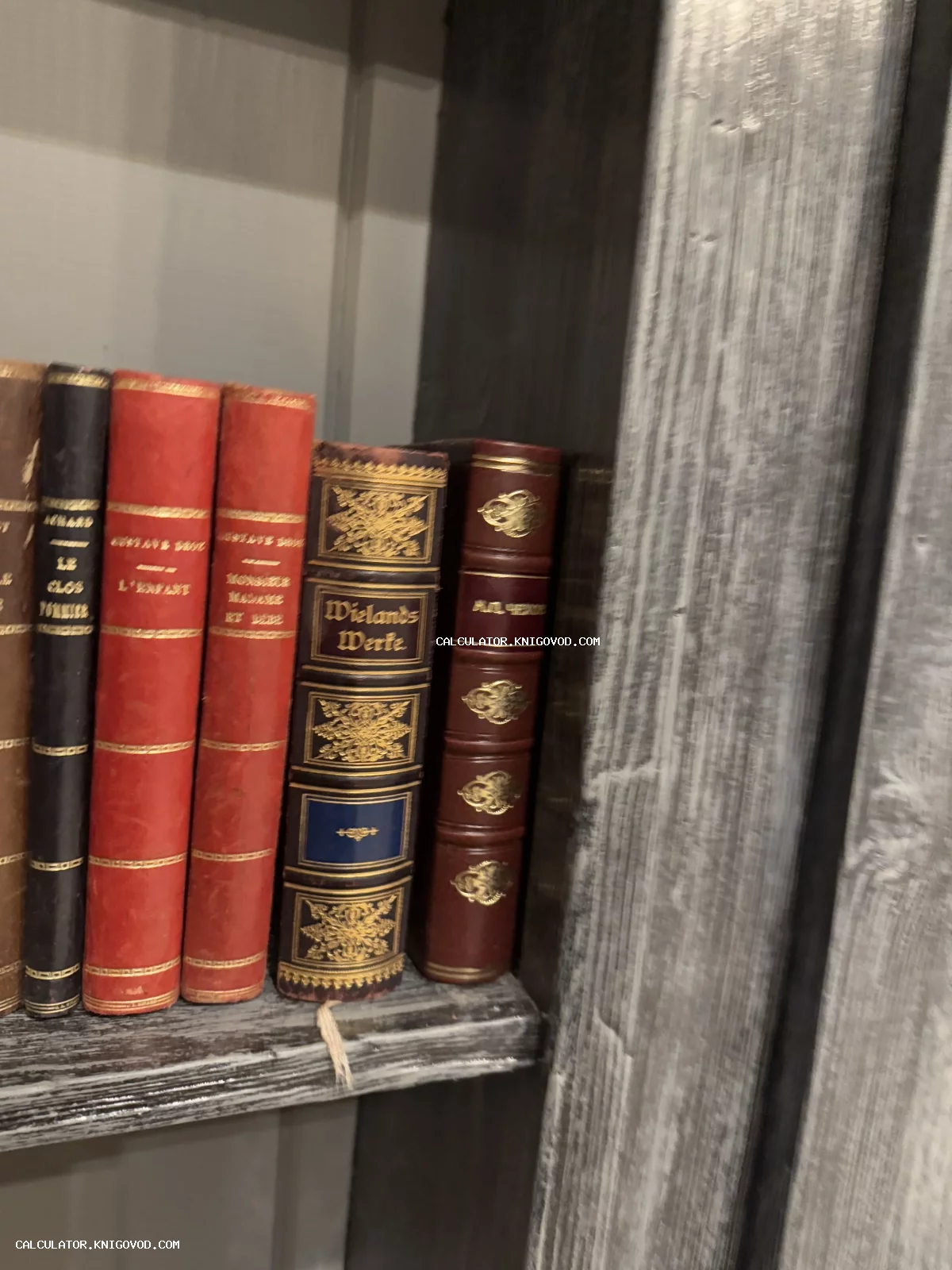 Корешки старинных книг с золотым тиснением на деревянной полке, включая издание произведений Виланда.