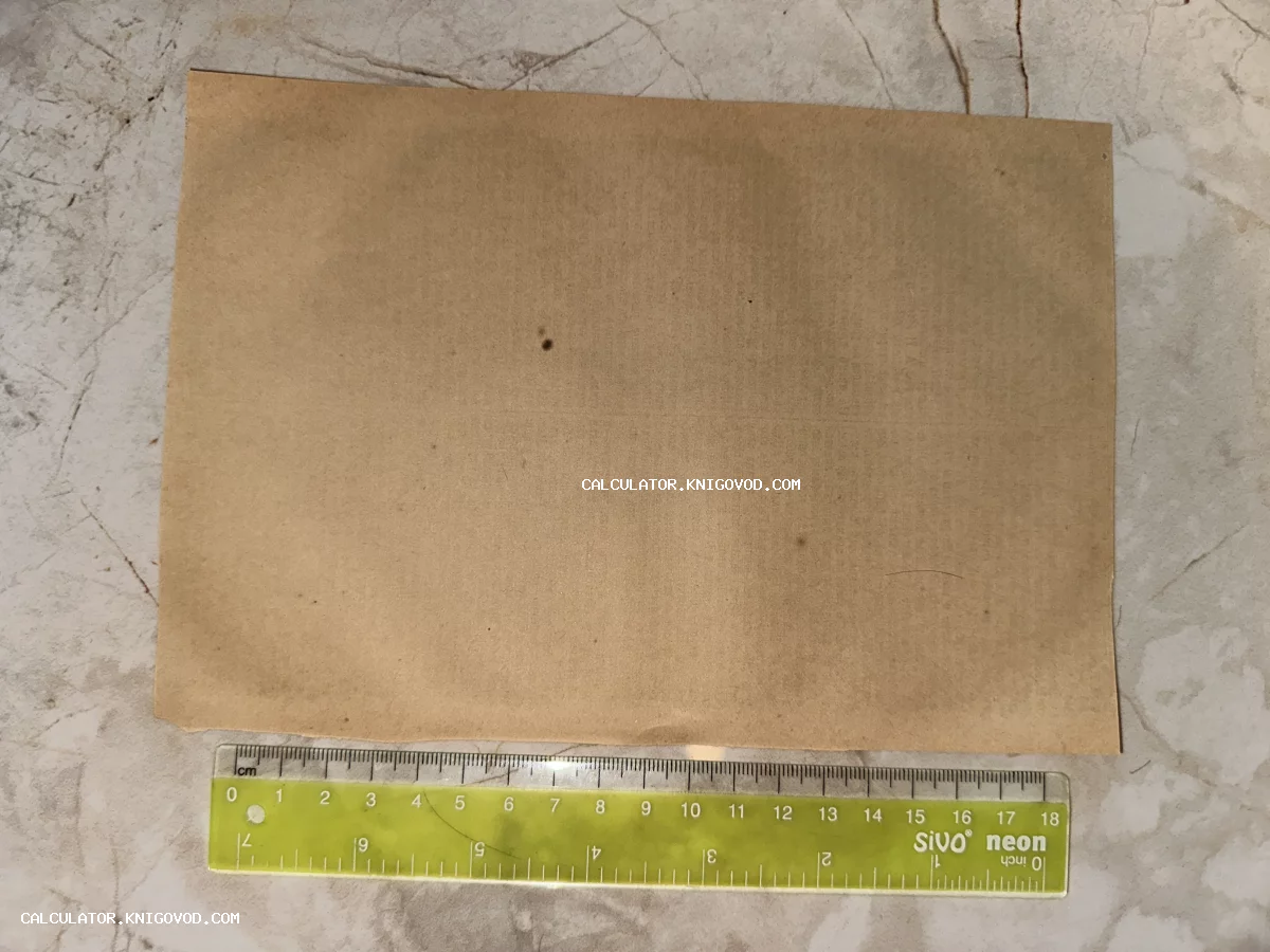 Оборотная сторона старинного пожелтевшего листа бумаги с пятнами времени, лежащая рядом с измерительной линейкой.