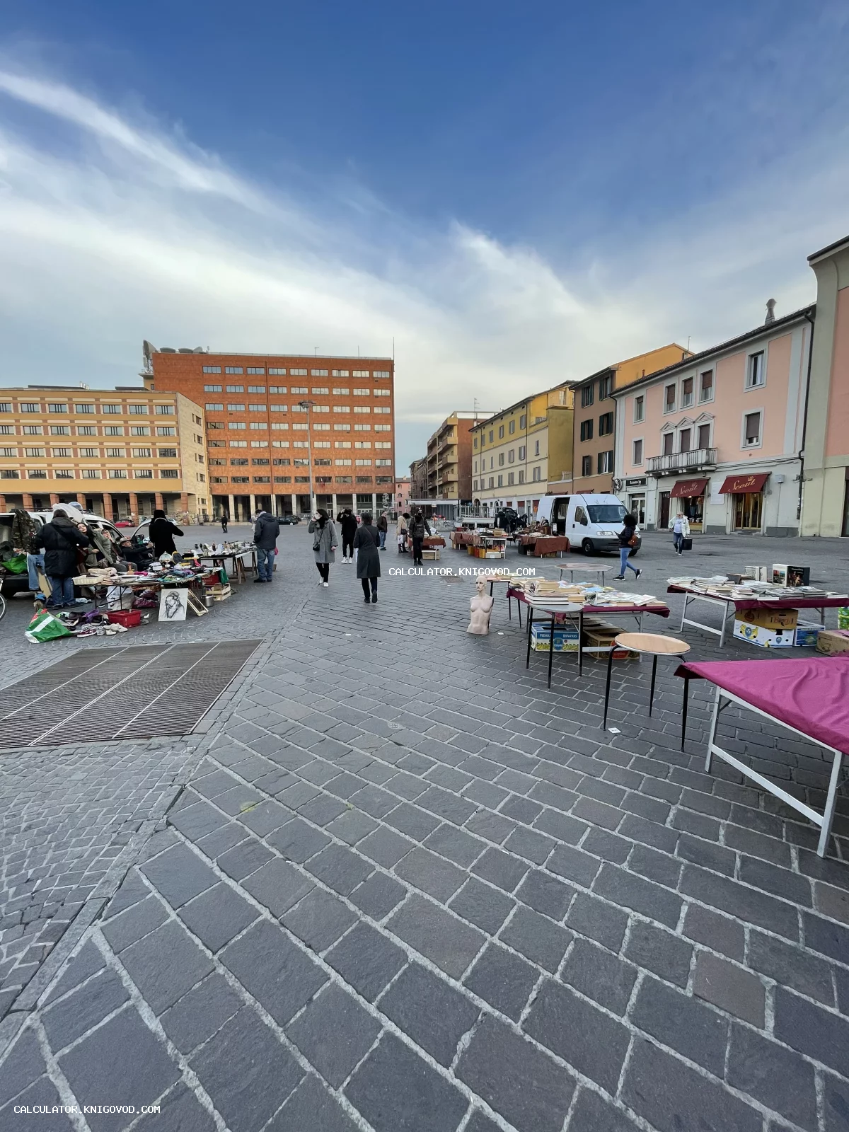 Вид на открытый антикварный рынок на мощеной площади города с прилавками старинных книг и предметов быта.