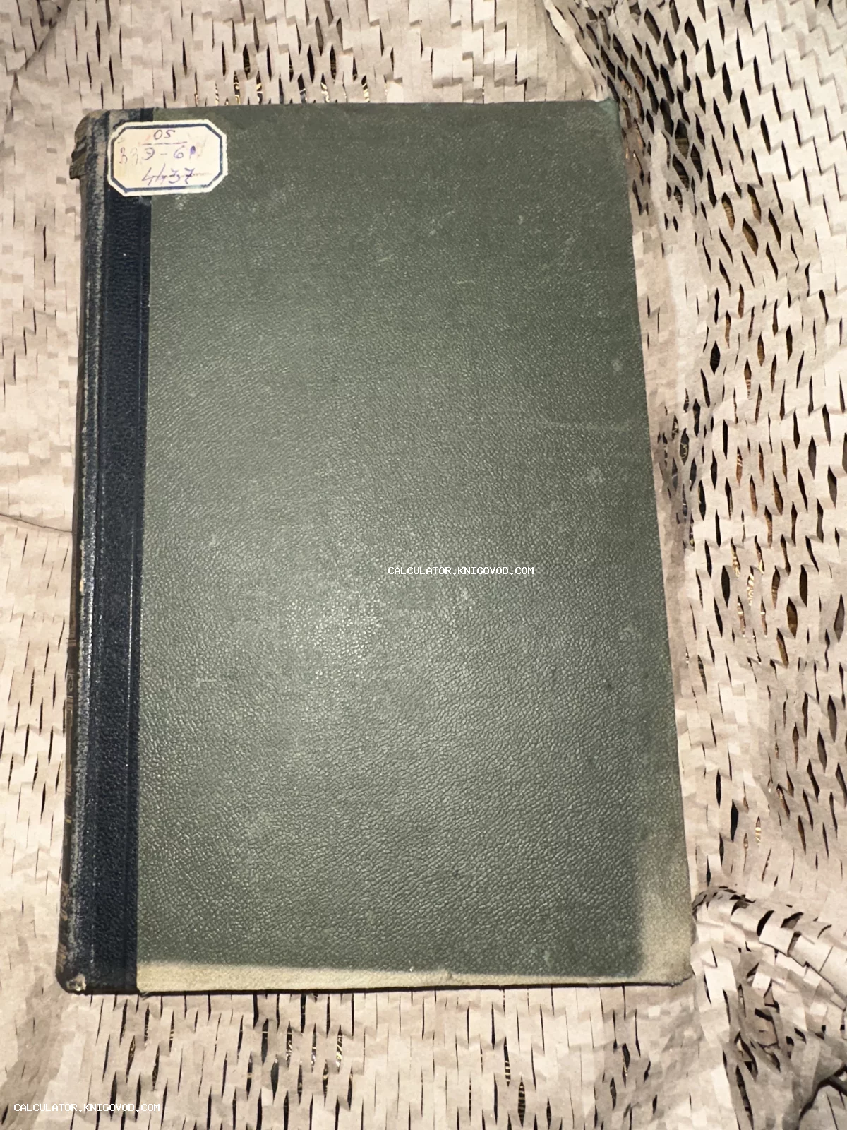 Старинная книга с темно-зеленой фактурной обложкой, черным корешком и архивной наклейкой на фоне упаковочной бумаги