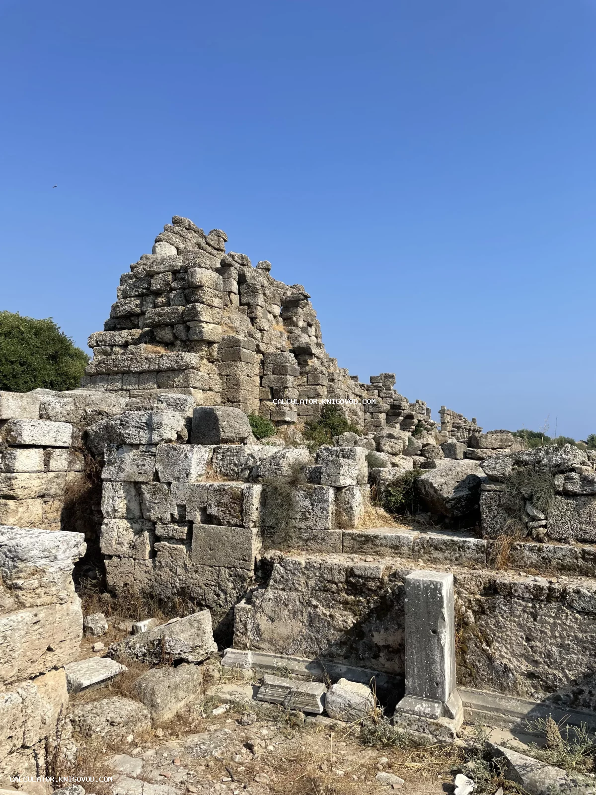 Массивные каменные блоки и разрушенные стены древнего античного сооружения под ясным синим небом.