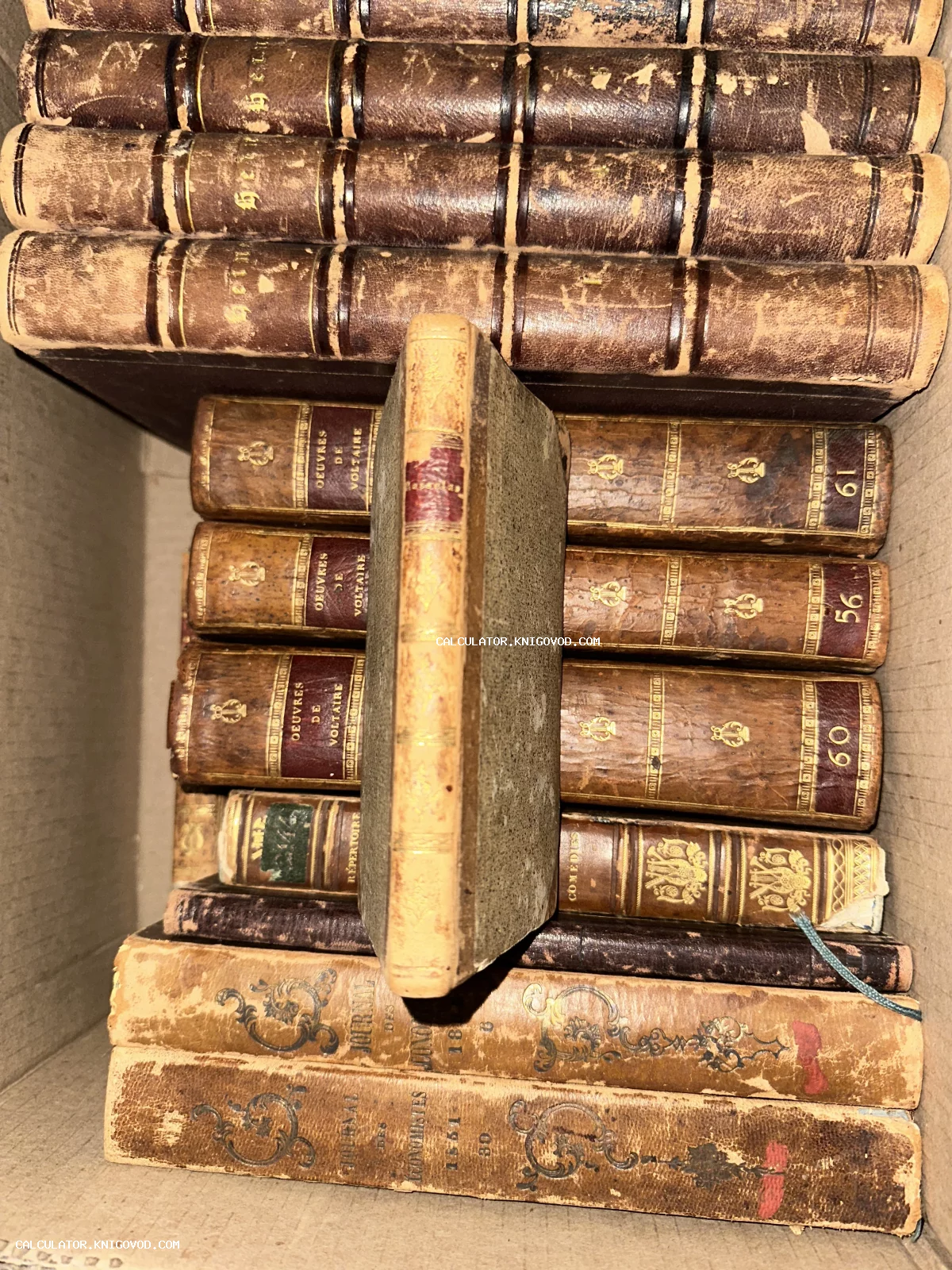 Старинные книги в кожаных переплетах с золотым тиснением, включая труды Вольтера, сложенные в коробке.