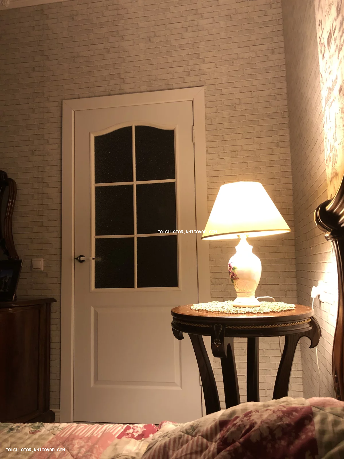 Интерьерная настольная лампа с керамическим основанием на круглом резном столике в уютной спальне.