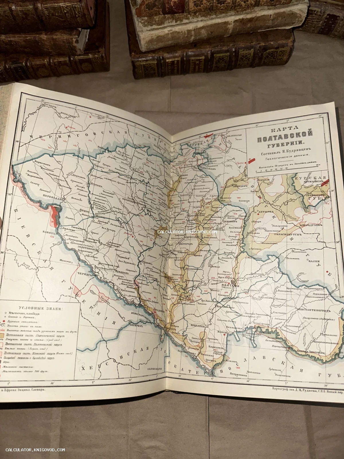 Разворот старинной книги с цветной геологической картой Полтавской губернии на фоне стопки антикварных фолиантов.