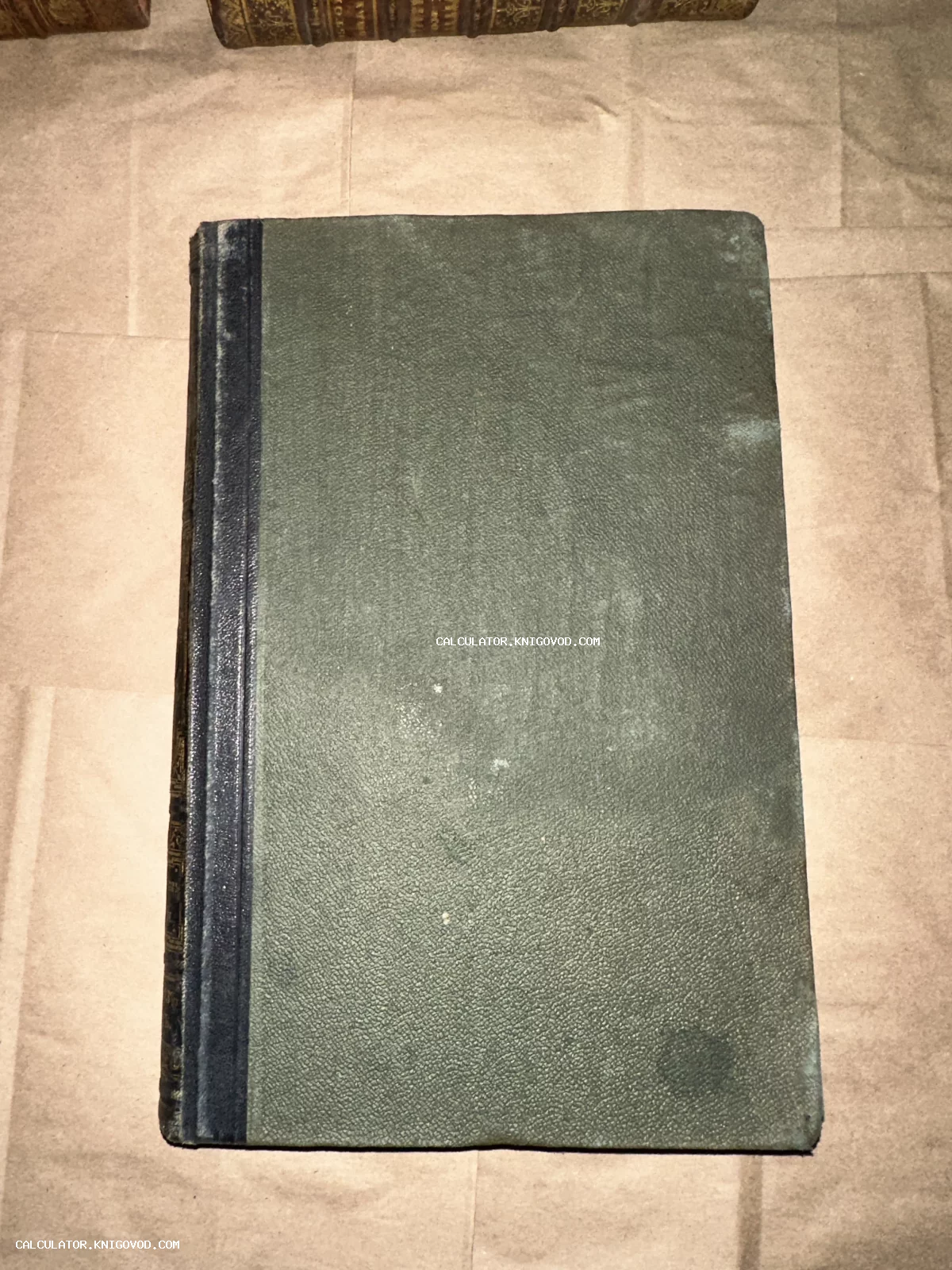 Вид сверху на антикварную книгу с зеленой фактурной обложкой и темным корешком, лежащую на крафтовой бумаге.