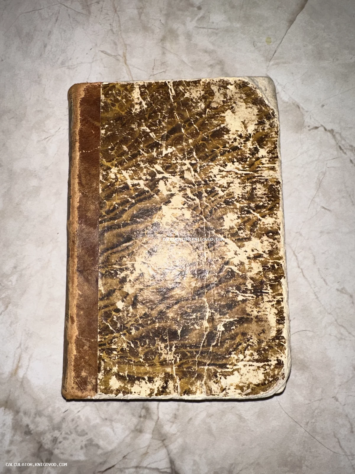 Старинная книга с потертой мраморной обложкой и кожаным корешком на светлой поверхности