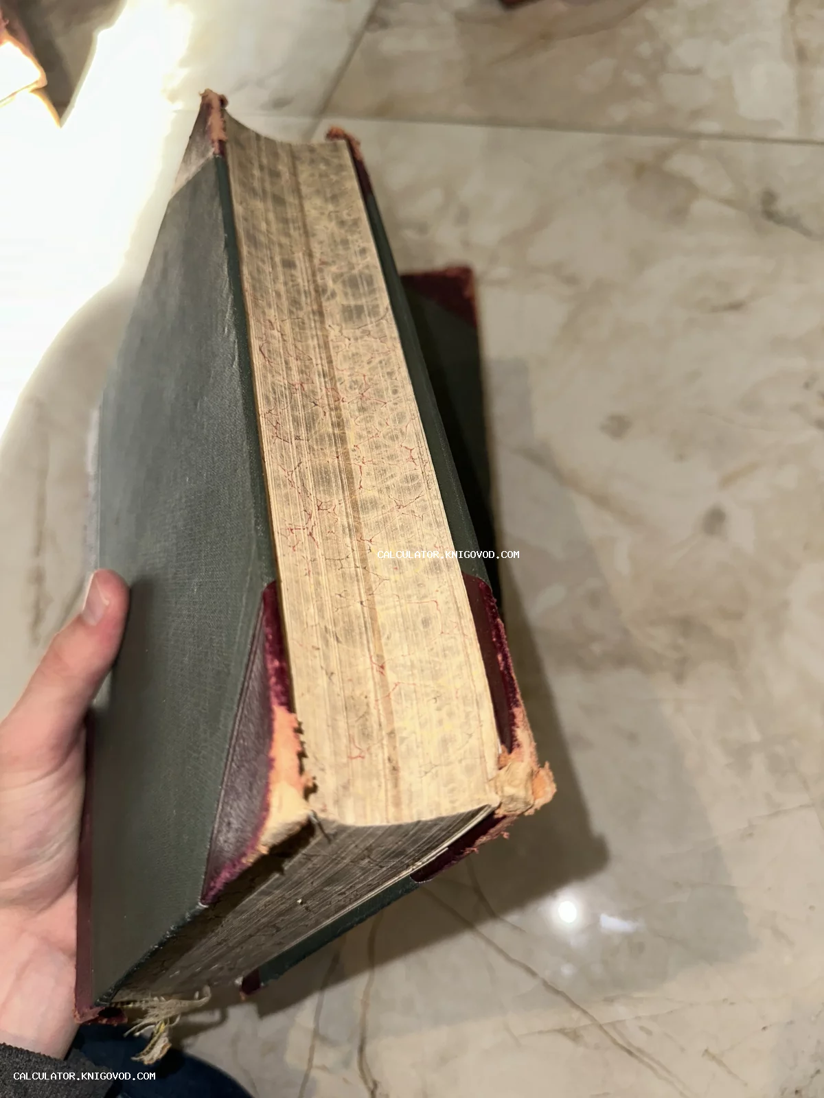 Вид на книжный блок старинной массивной книги с мраморным рисунком на срезе и потертыми углами переплета.