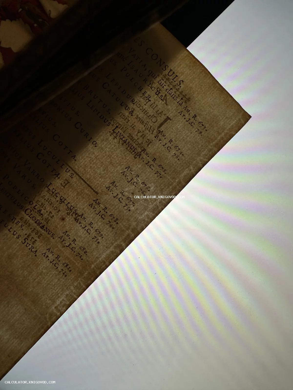 Макросъемка страницы старинной книги с именами римских консулов на французском языке под радужным преломлением света.