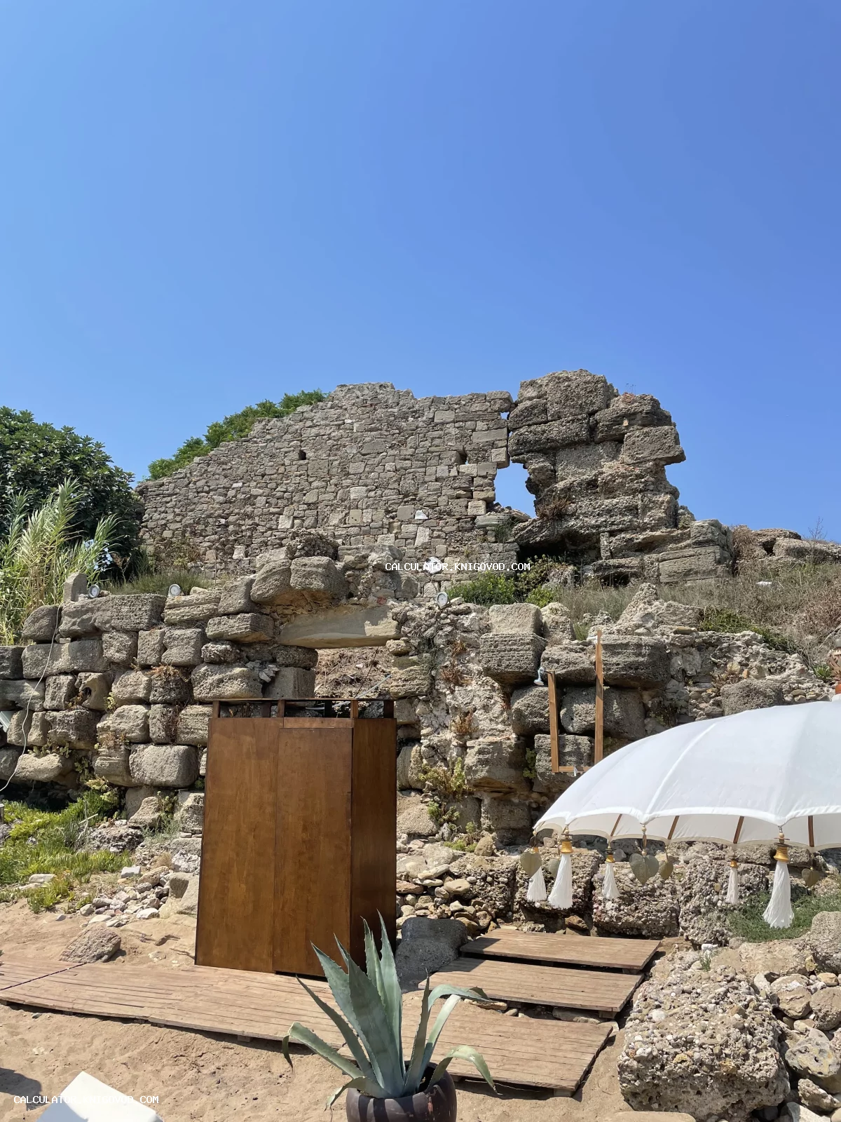 Массивная стена из грубого дикого камня, являющаяся частью древних руин, на фоне ярко-синего неба.