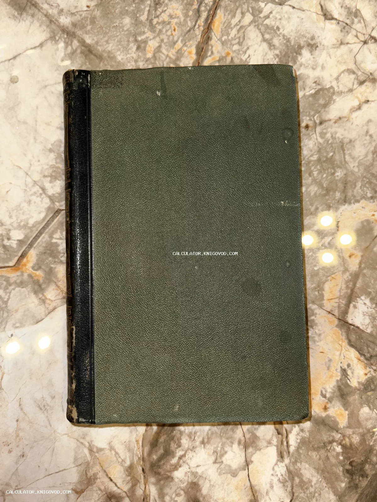 Старинная книга с темно-зеленой текстурированной обложкой и черным кожаным корешком на мраморном столе.