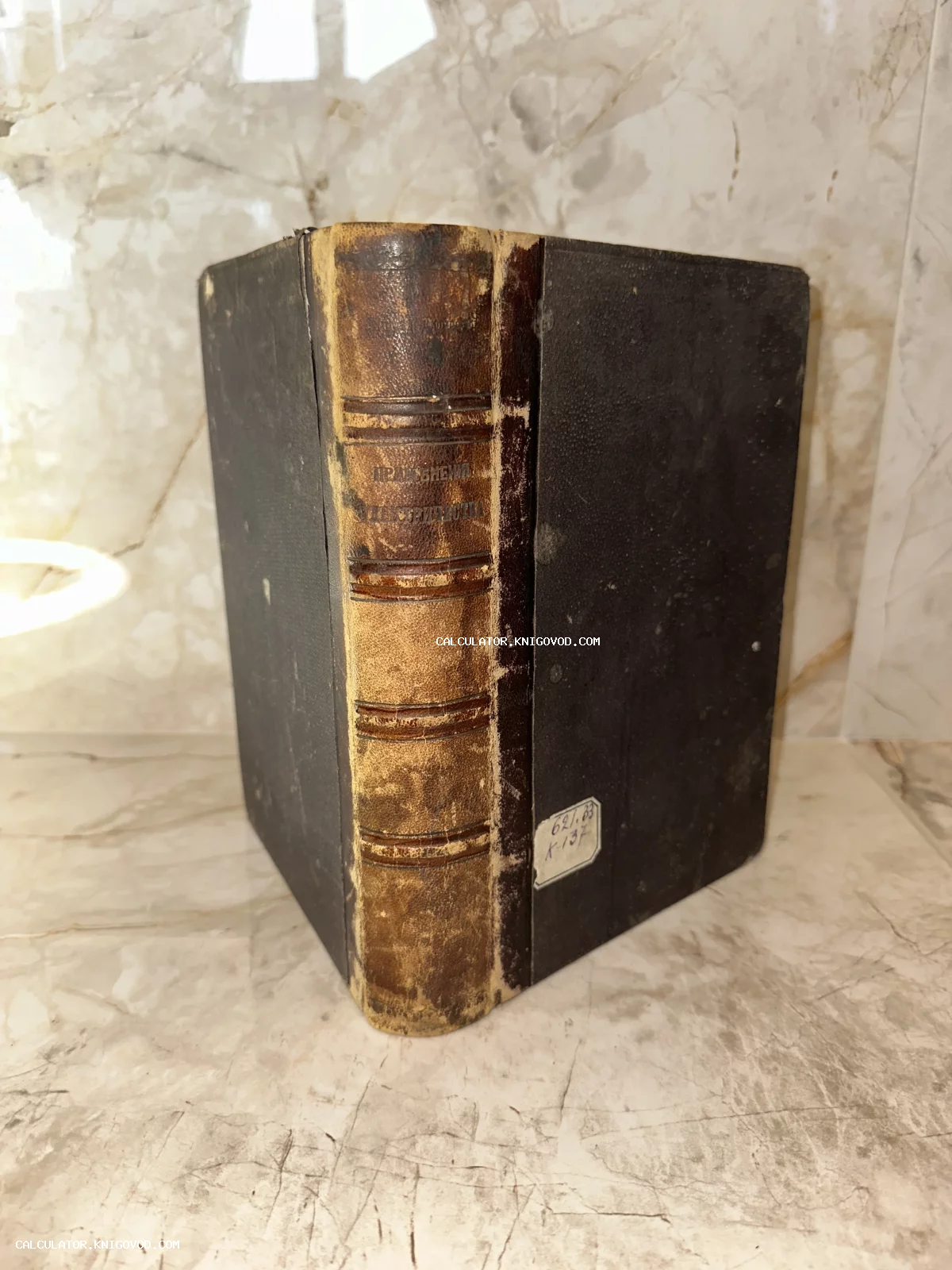 Массивная антикварная книга с потертым кожаным корешком и темной обложкой на мраморном фоне.