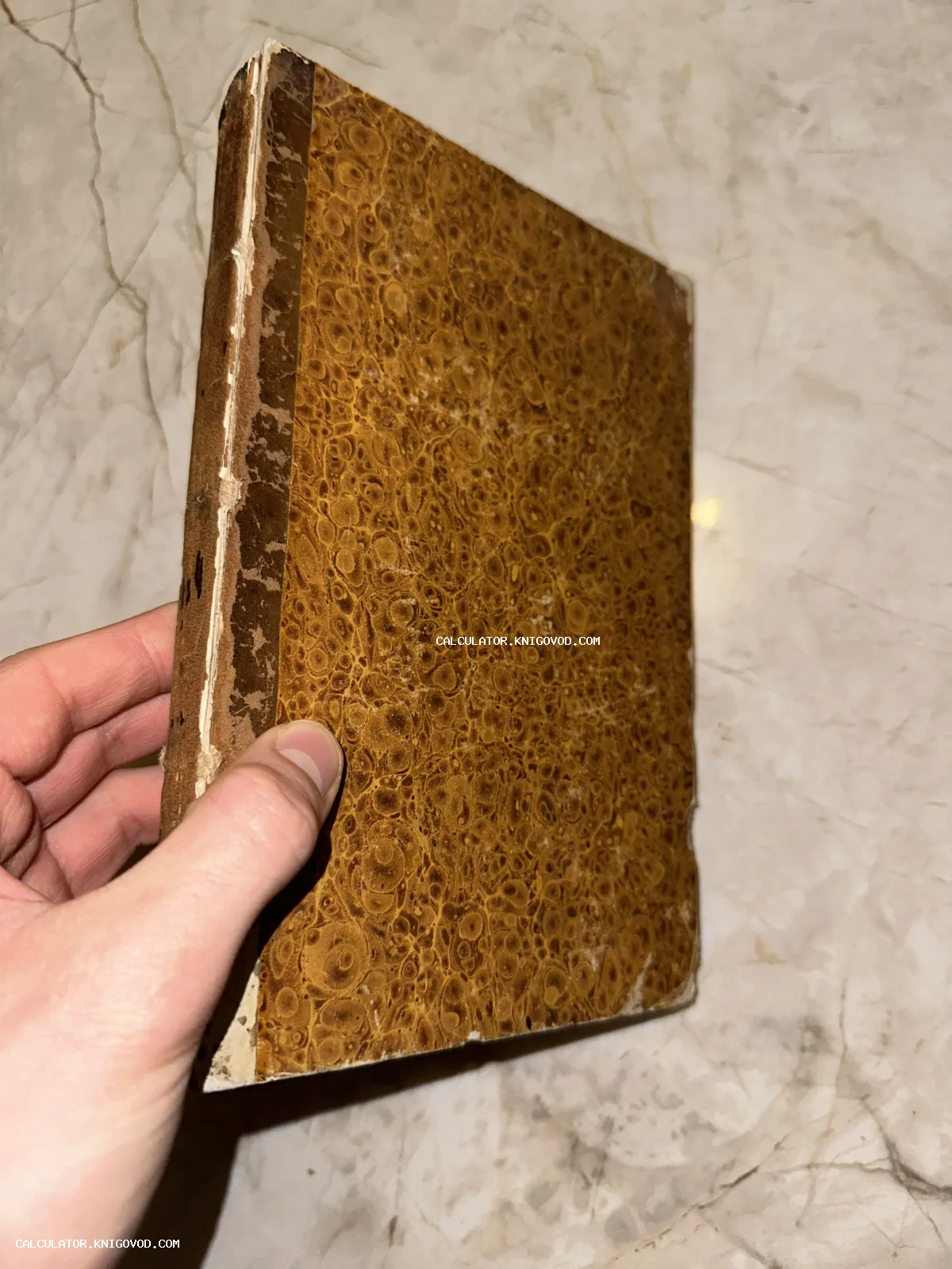 Старинная книга в твердом переплете с характерным мраморным узором охристого цвета, вид сбоку.