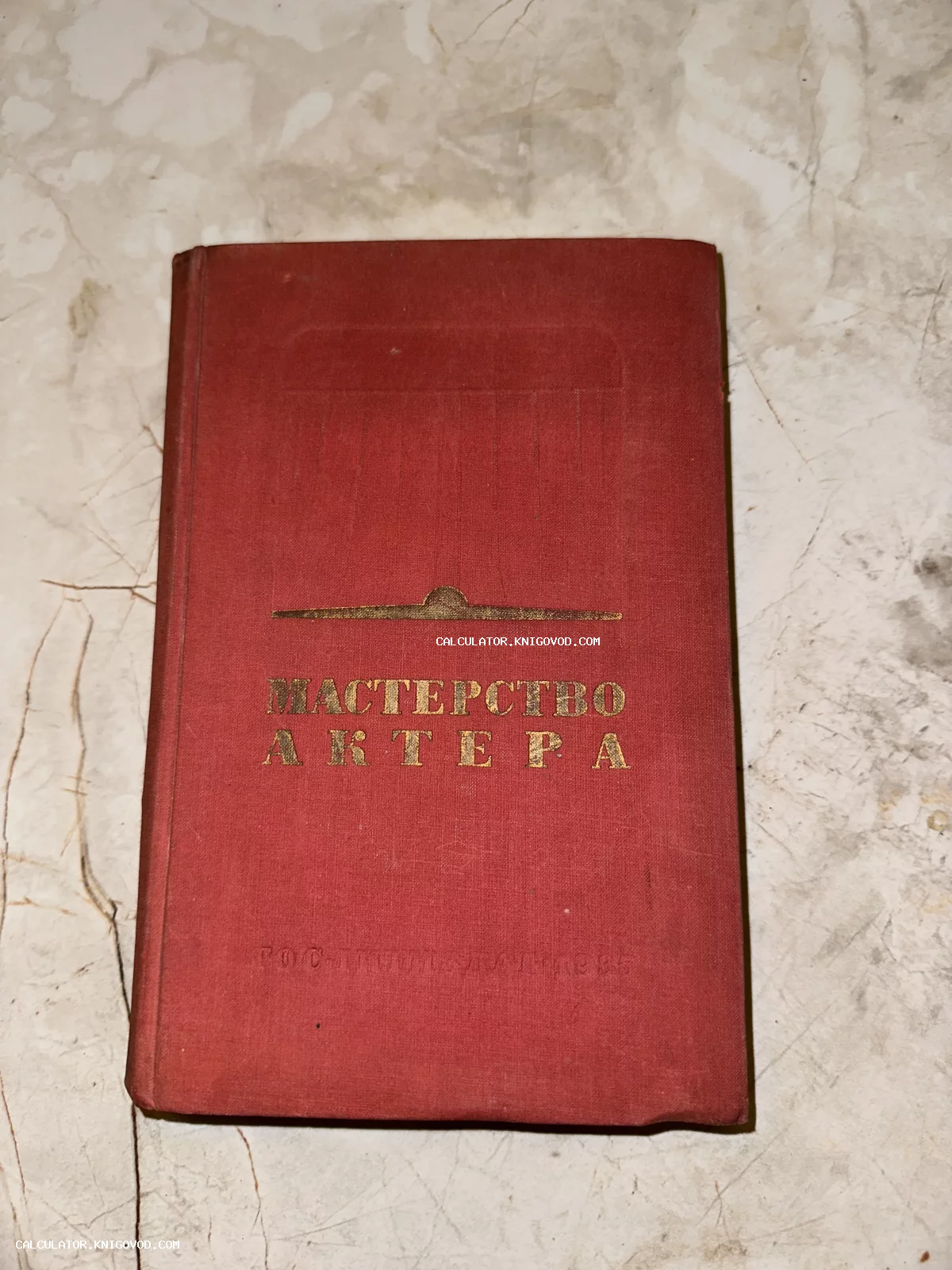 Старая книга в красном тканевом переплете с золотым тиснением «Мастерство актера» на мраморной поверхности.