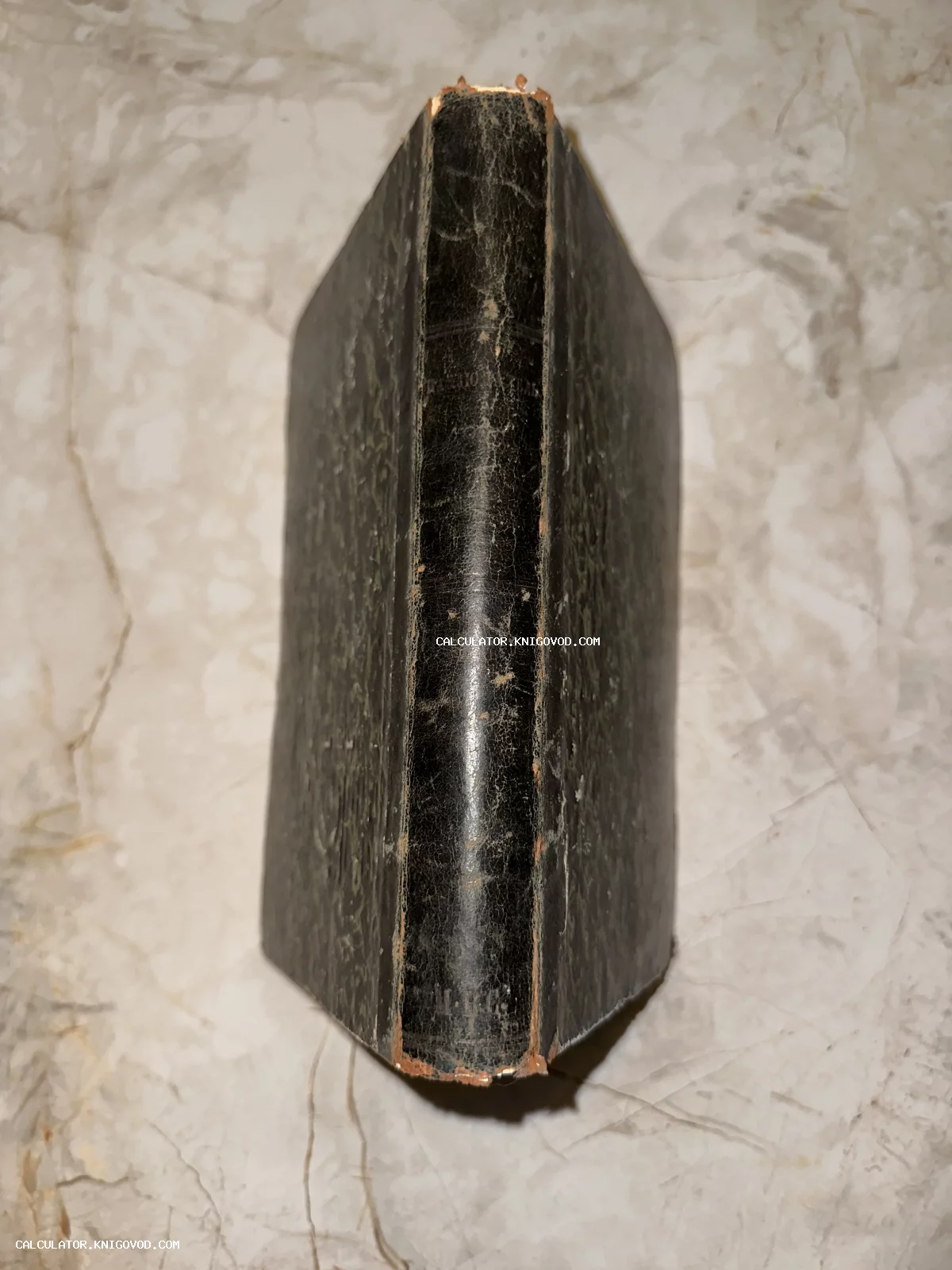 Вид сверху на корешок и обложку старинной антикварной книги с потертостями на светлом мраморном фоне.