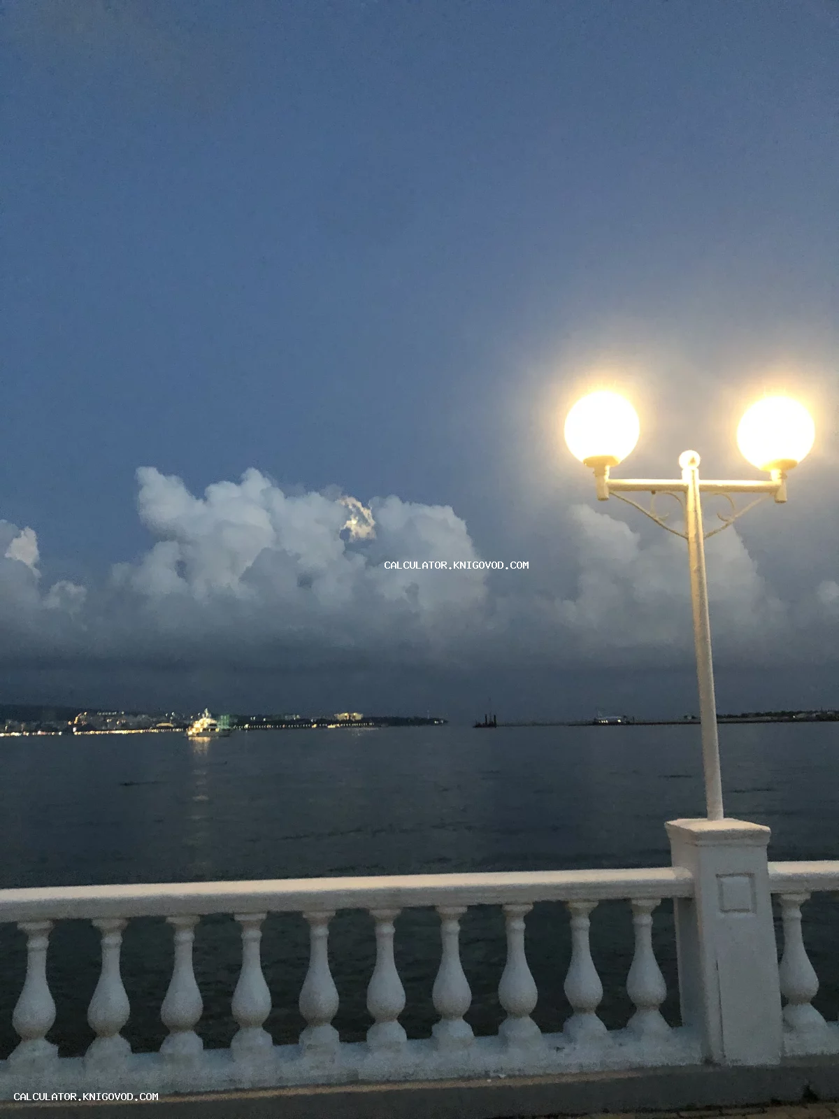 Вид на море через белую балюстраду с горящим двухрожковым фонарем в сумерках.