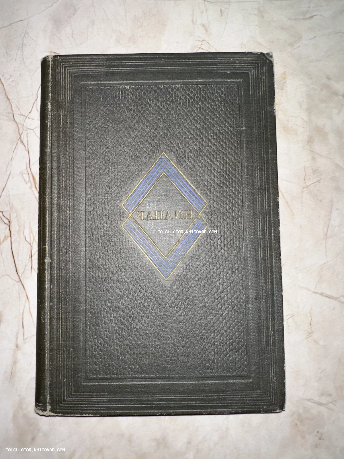Старая книга с темной фактурной обложкой и надписью «Чаплин» внутри золотисто-синего ромба.