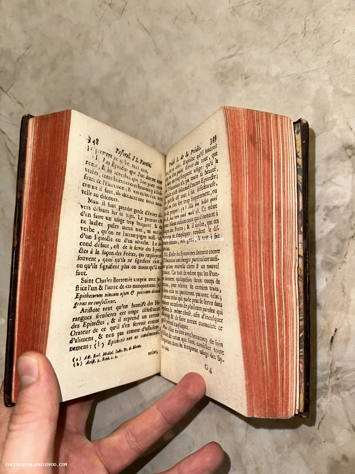 Раскрытая антикварная книга на французском языке с характерным красным тонированием обреза, удерживаемая рукой.