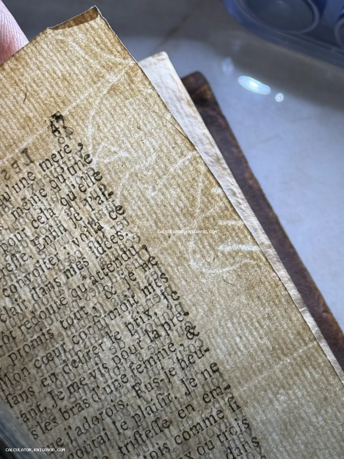 Крупный план старинной пожелтевшей книжной страницы с французским текстом и выраженной сетчатой фактурой бумаги.