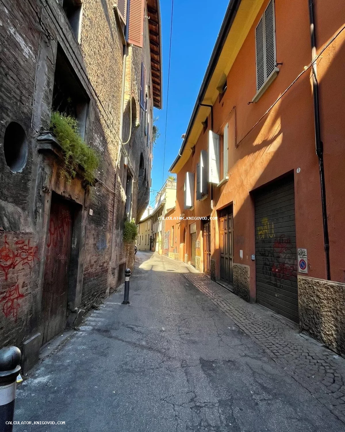 Вид на узкий старинный переулок с кирпичными и оранжевыми зданиями, залитый солнечным светом под синим небом.