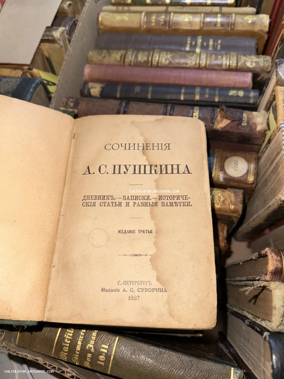Разворот антикварной книги А. С. Пушкина 1887 года издания с титульным листом на фоне других старинных томов.