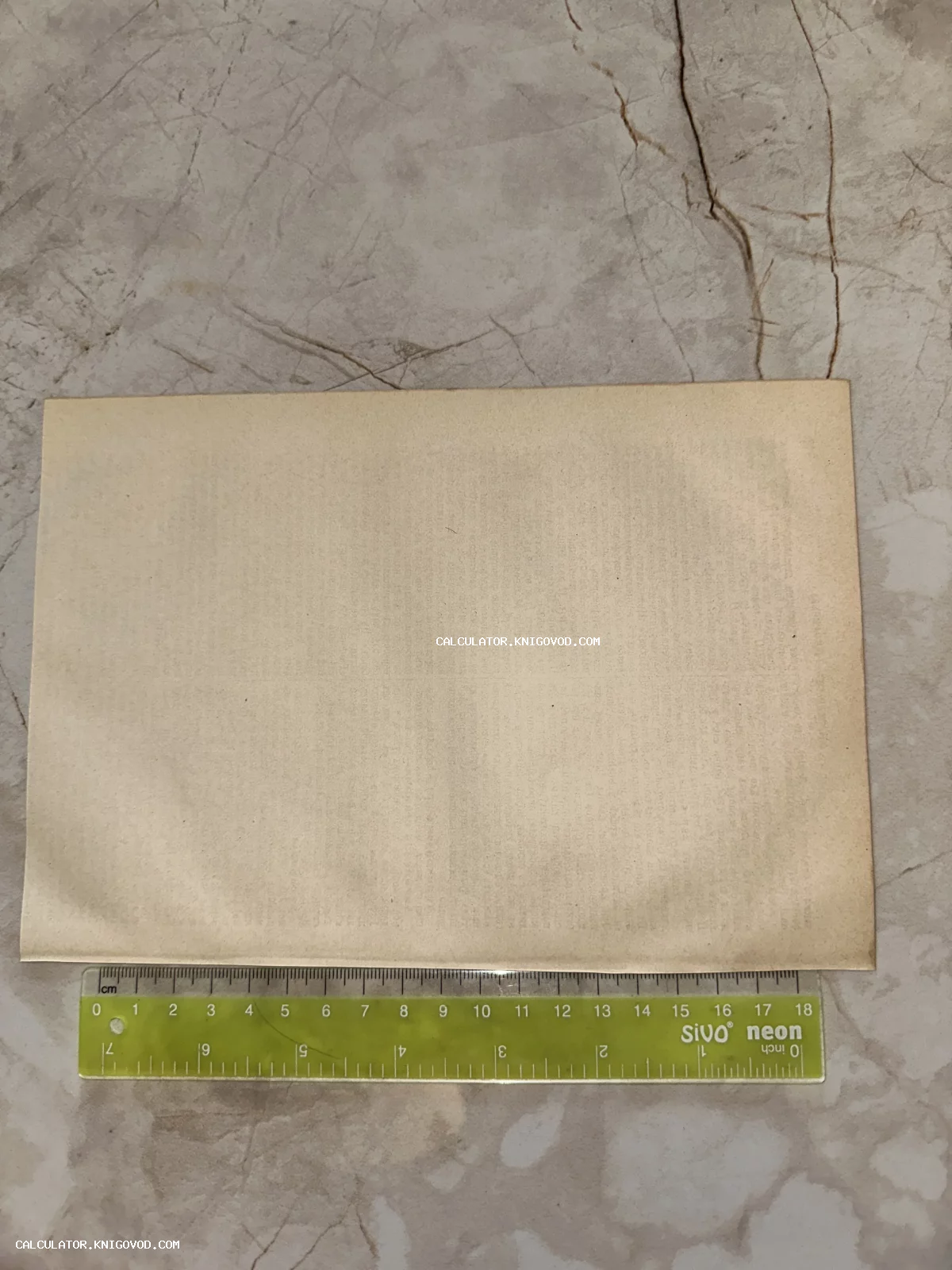 Оборотная сторона старинной пожелтевшей бумаги рядом с мерной линейкой на мраморном фоне.