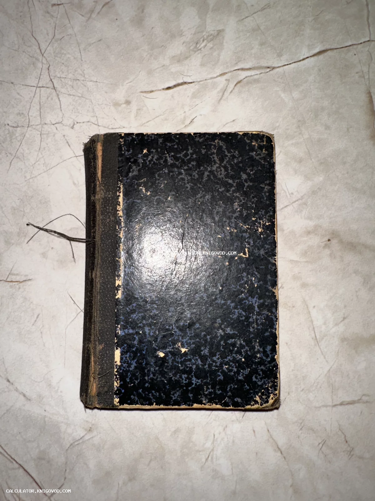 Вид сверху на старинную книгу или блокнот с темно-синей мраморной обложкой и сильно изношенным корешком на светлой поверхности.