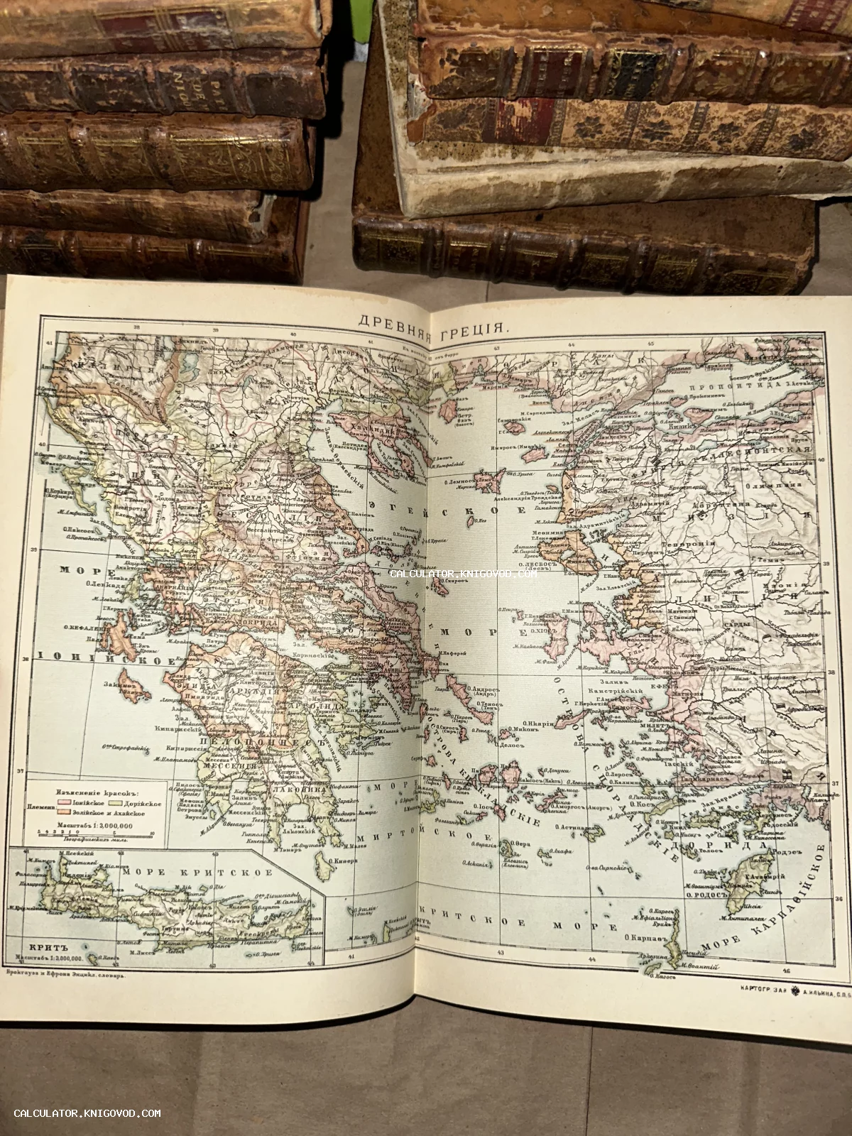 Старинная цветная карта Древней Греции на развороте книги, окруженная томами в кожаных переплетах.