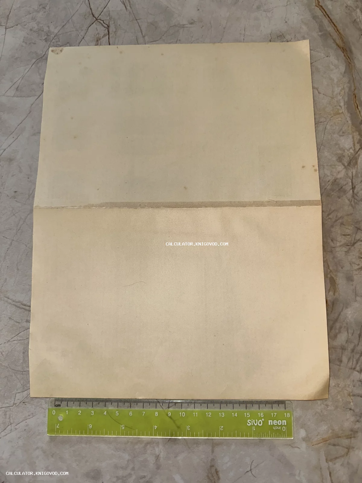 Старинный пожелтевший лист бумаги, вид сзади, с горизонтальным сгибом по центру и измерительной линейкой внизу.