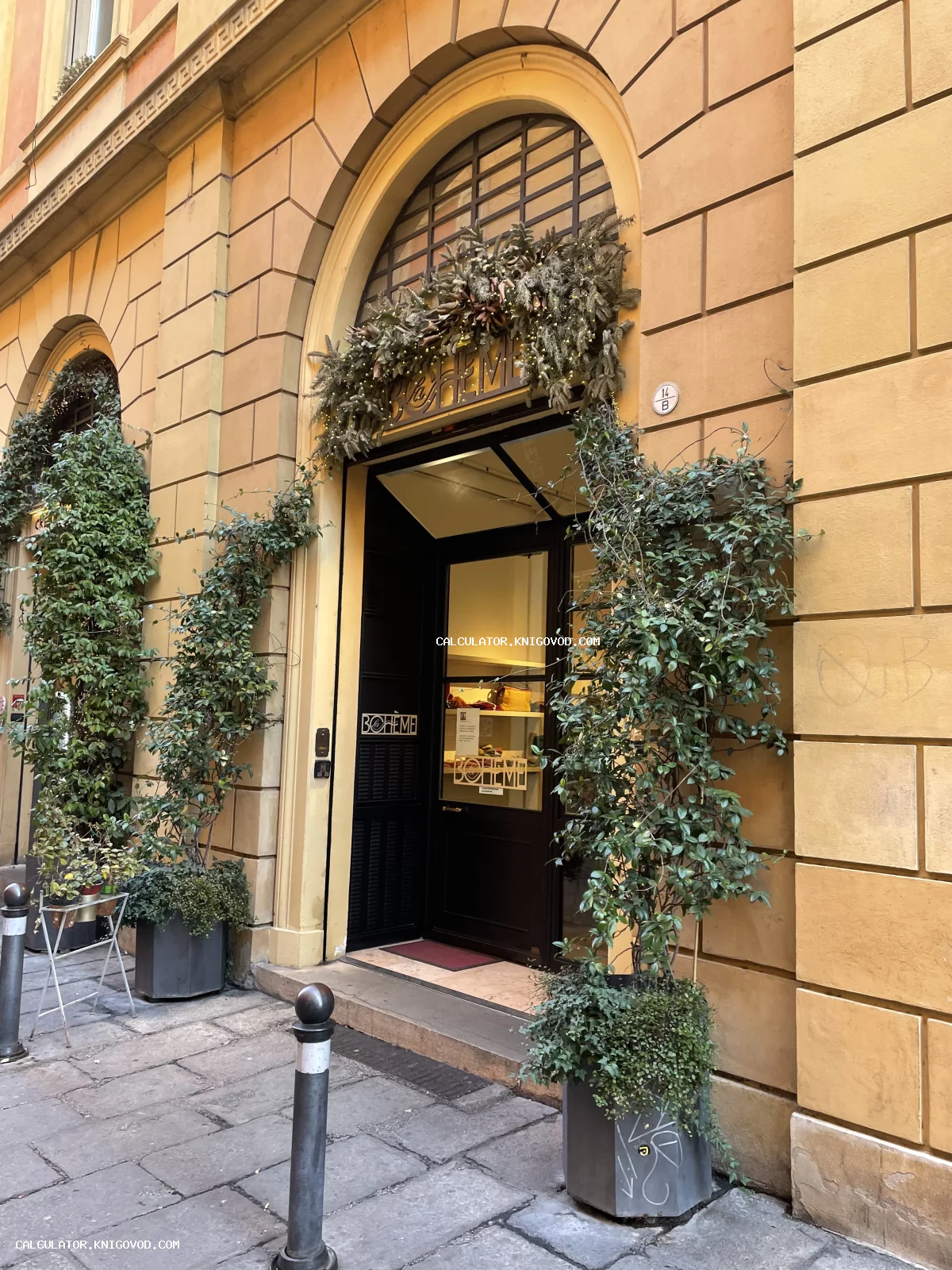 Арочный вход в магазин La Bohème в старинном желтом здании с декоративными растениями и праздничной гирляндой.