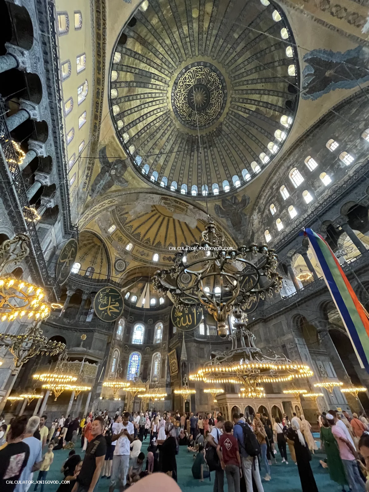 Взгляд изнутри на купол и люстры мечети Айя-София в Стамбуле с арабской каллиграфией и византийскими элементами.