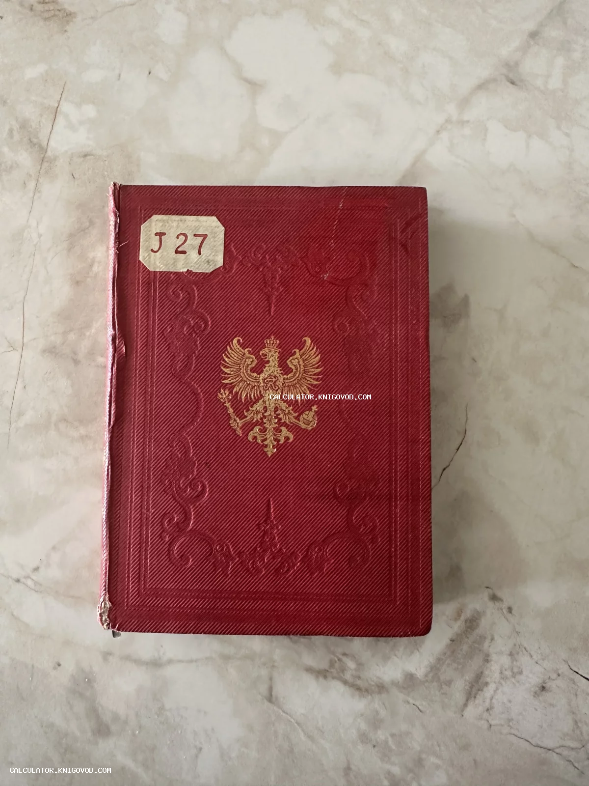 Старинная книга в красном коленкоровом переплете с золотым тиснением двуглавого орла и библиотечной меткой.