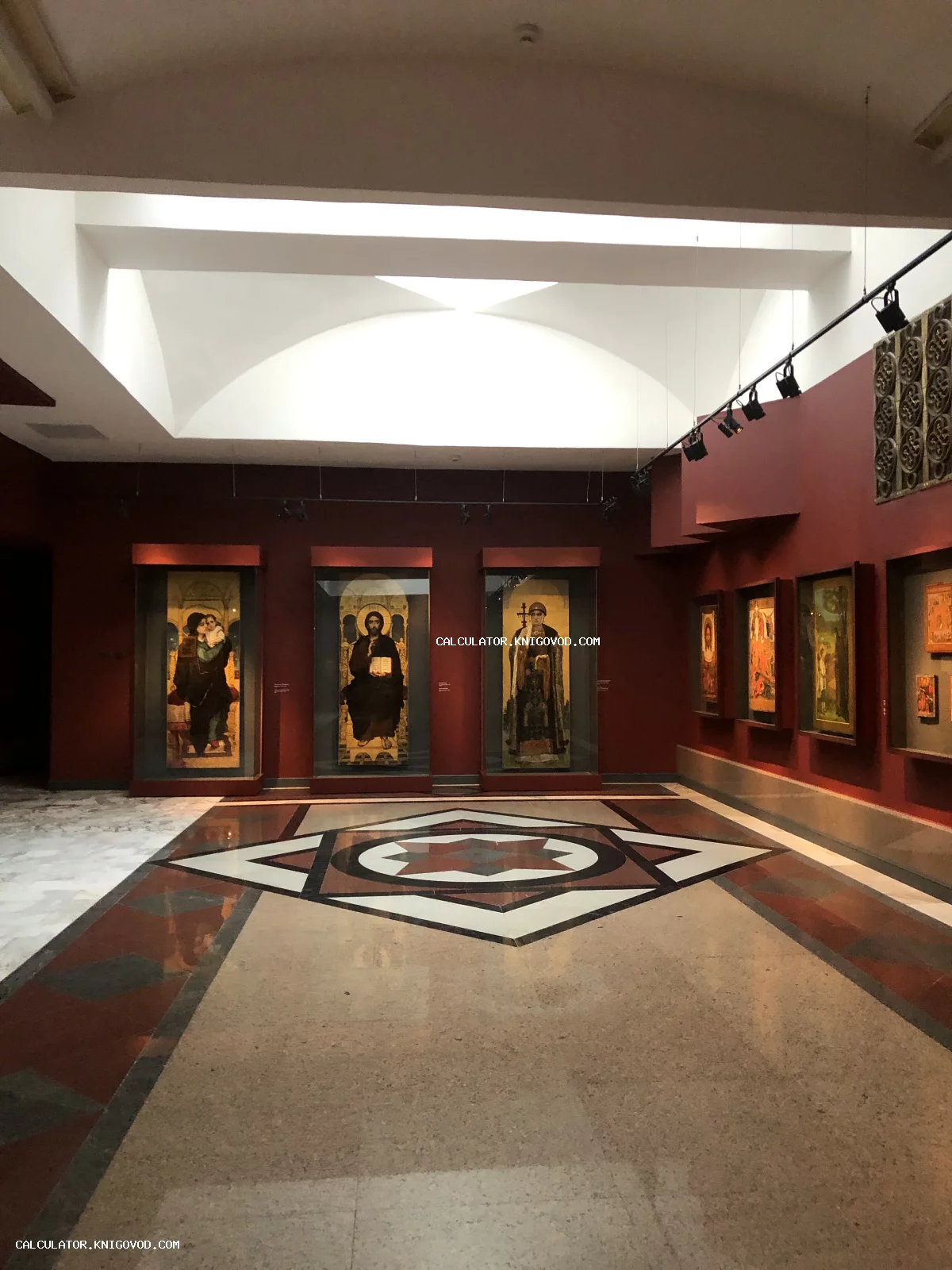 Интерьер музейного зала с темно-красными стенами и старинными высокими иконами в нишах под стеклом.