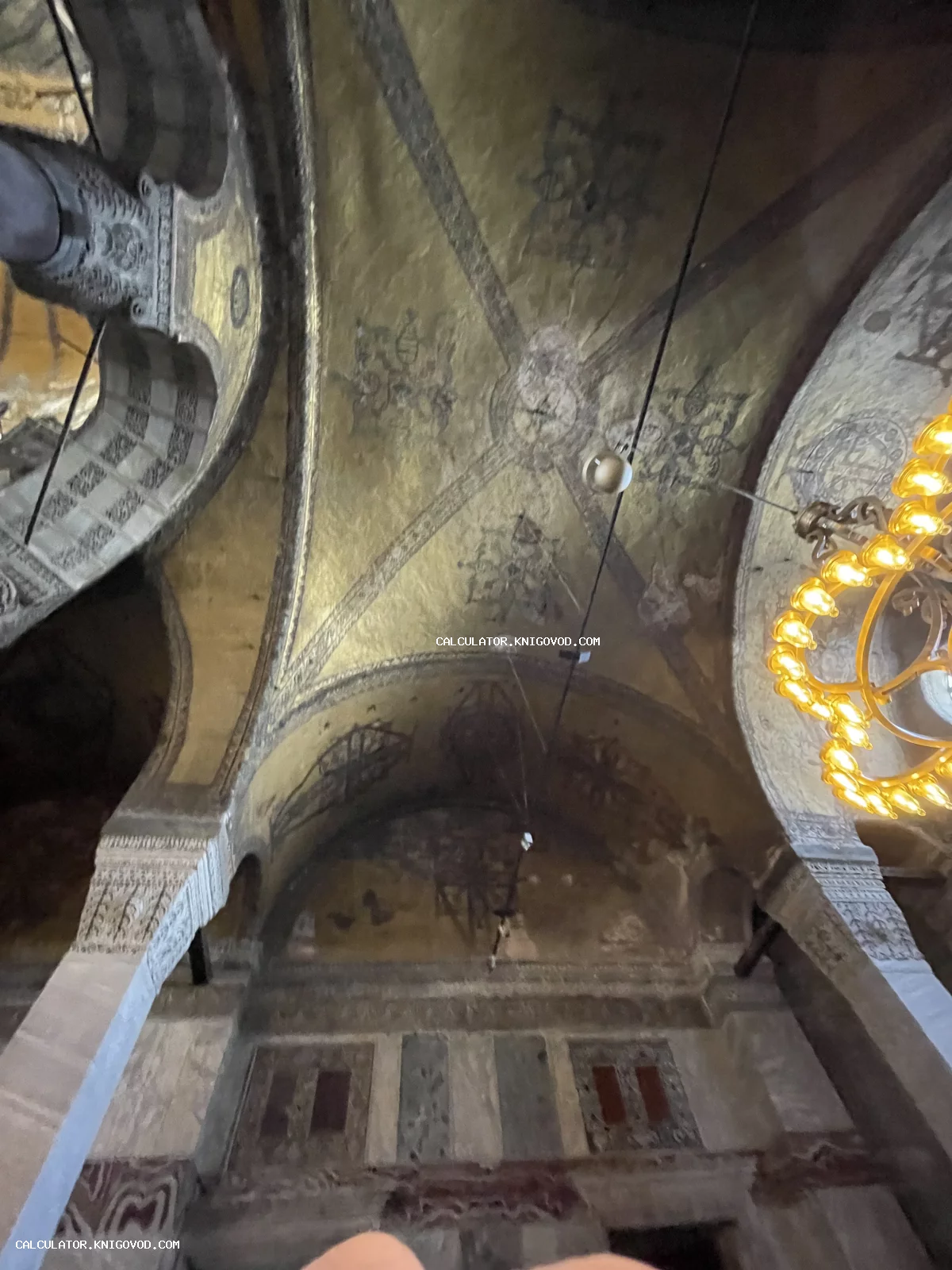 Вид снизу на золотые мозаичные своды, массивные арки и светящуюся люстру в интерьере древнего храма.