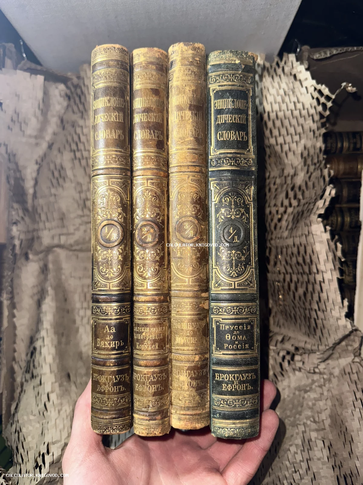 Четыре тома антикварного Энциклопедического словаря Брокгауза и Ефрона с золотым тиснением на корешках в руке человека.
